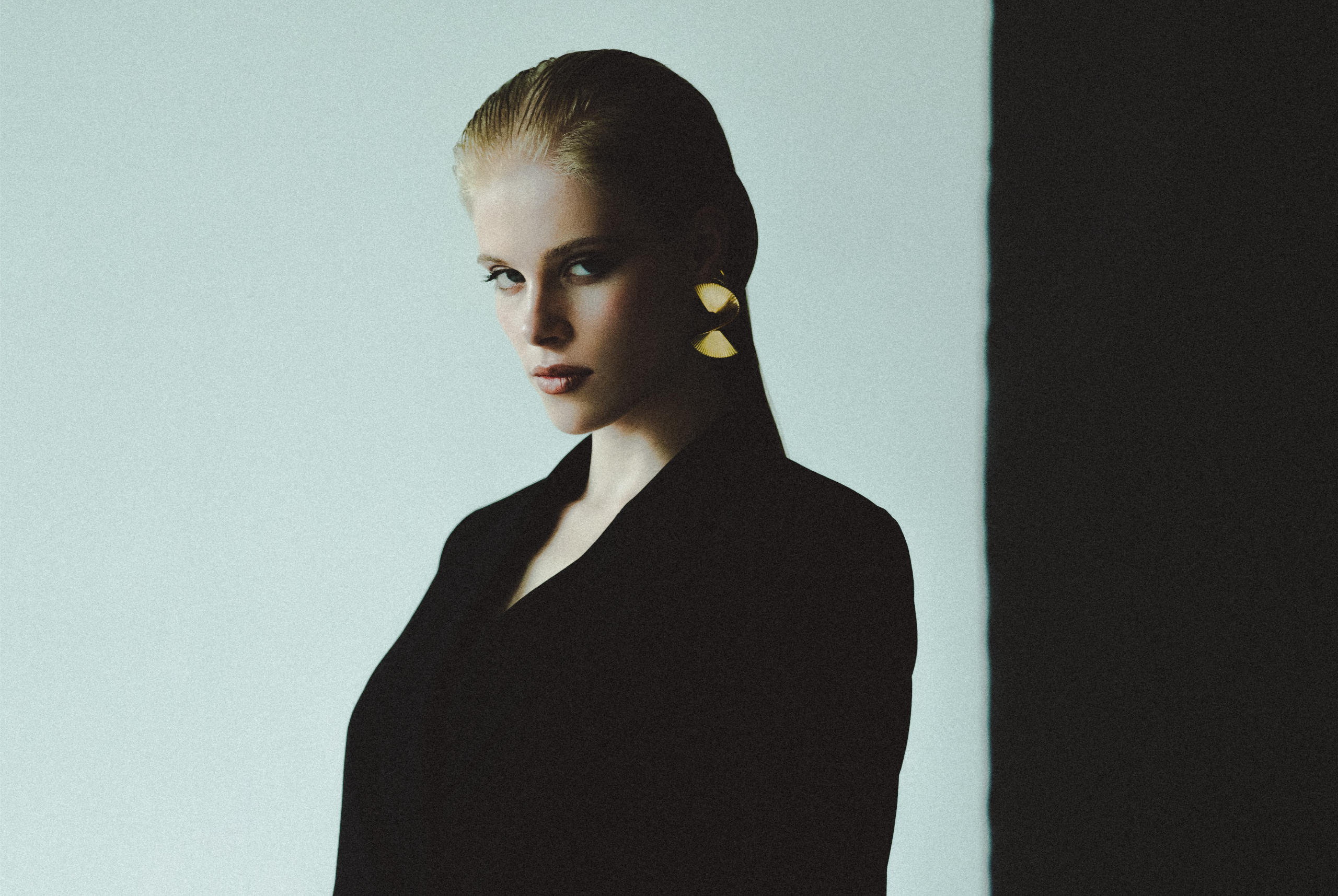 Elegant woman in black blazer with stylish gold earrings, posing in dramatic lighting.