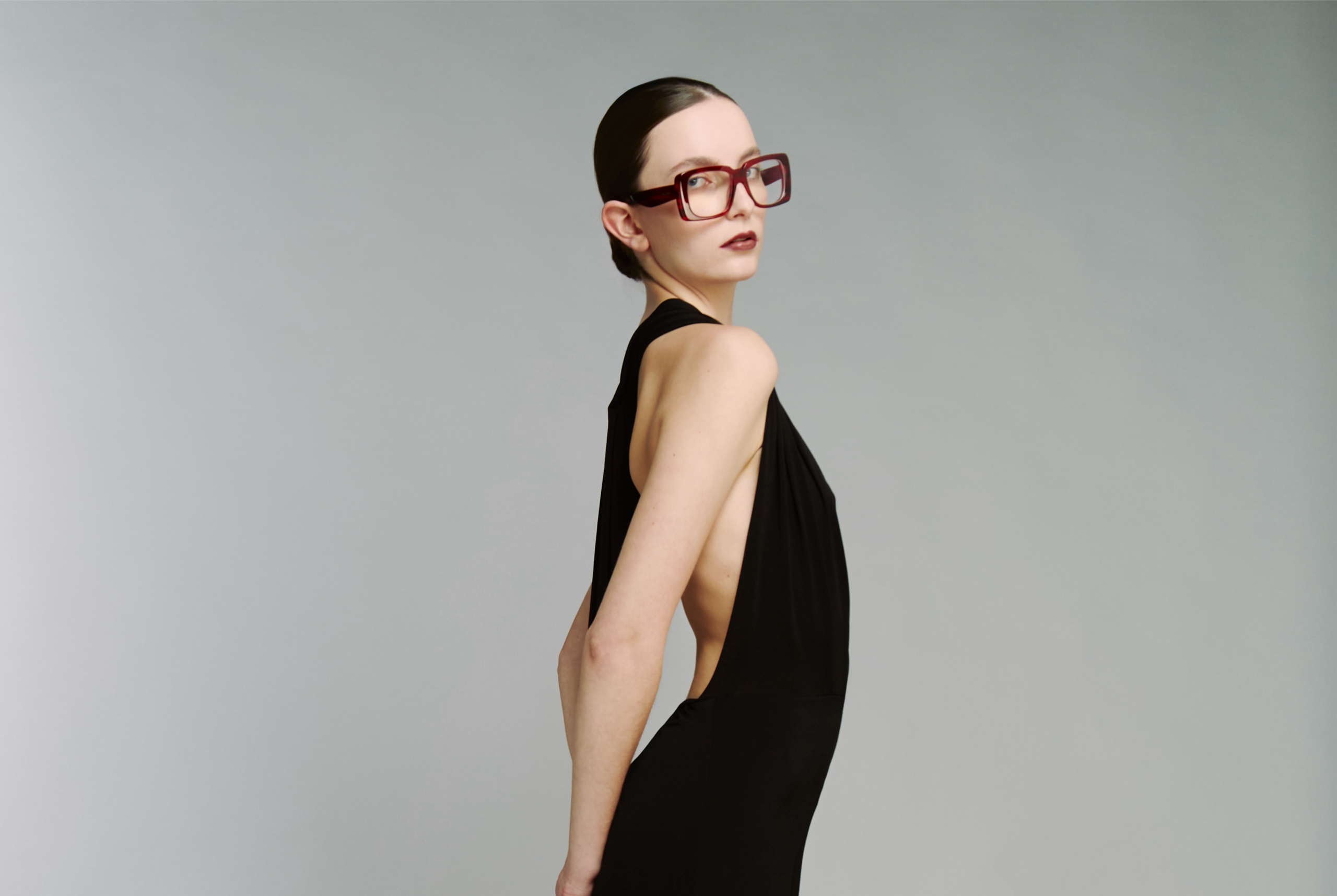 Fashion model in black dress, large glasses, striking pose in studio setting.