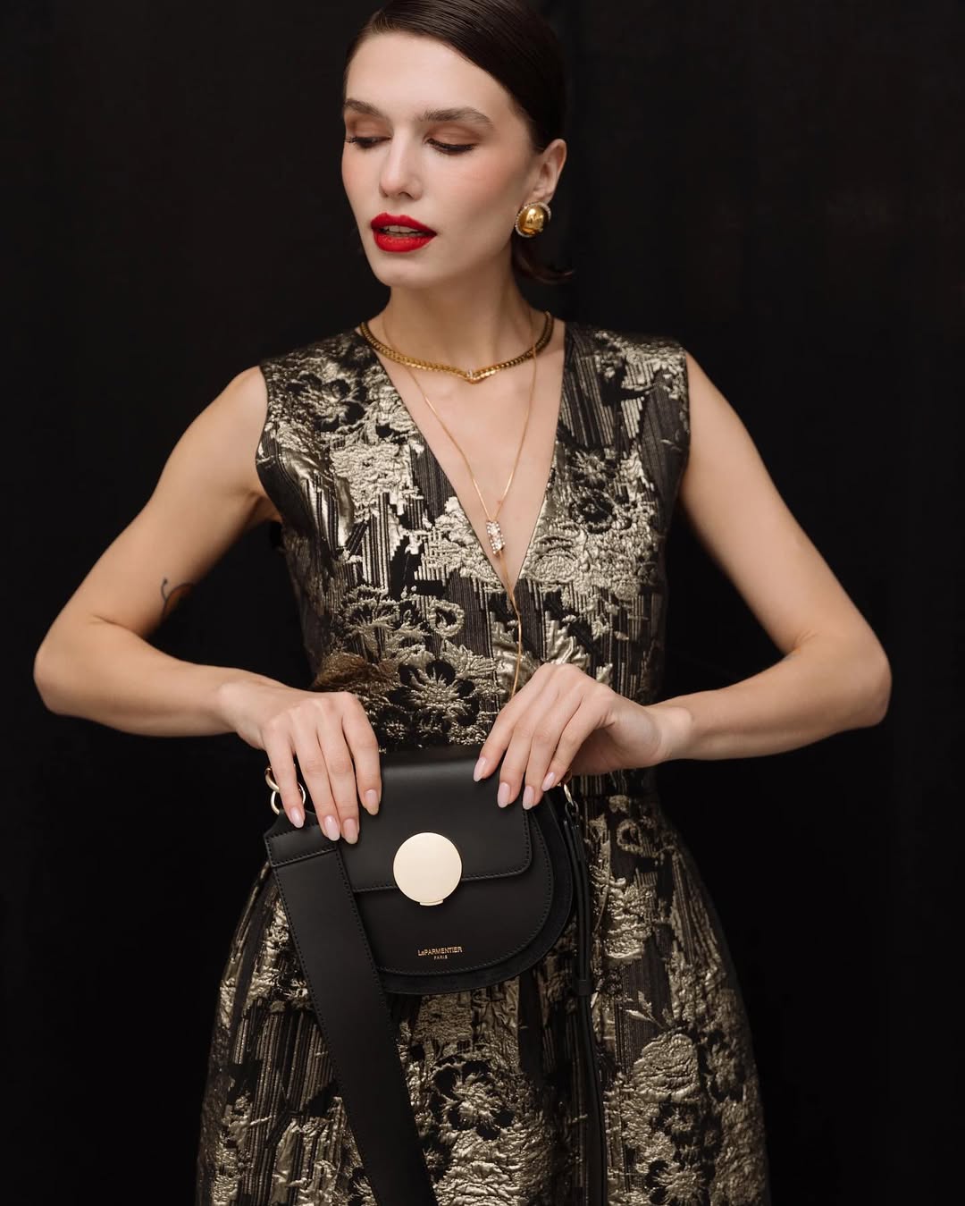 Elegant woman in floral dress holding chic black handbag against dark background.