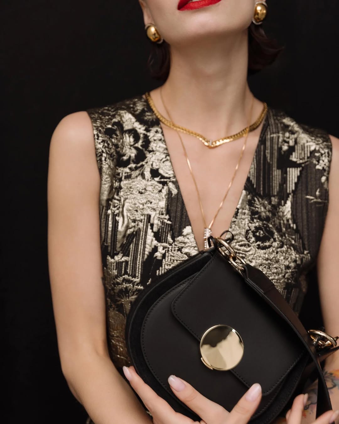 Elegant woman in gold print dress holding a stylish black handbag with gold accents.