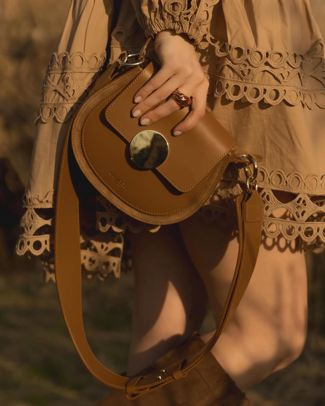 Elegant tan handbag and lace dress in stylish outdoor setting.