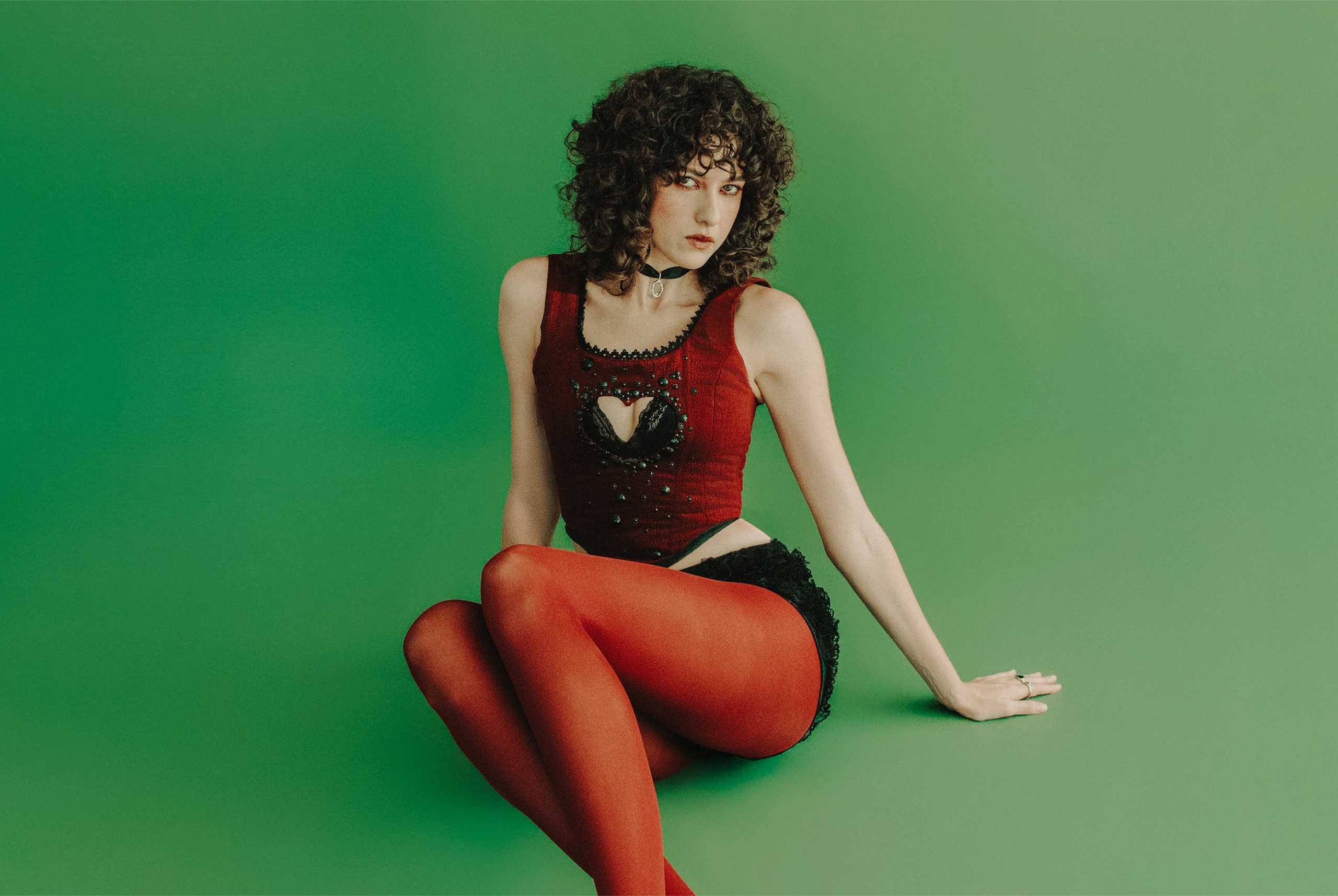 Stylish woman in red tights and top sitting on a green background.