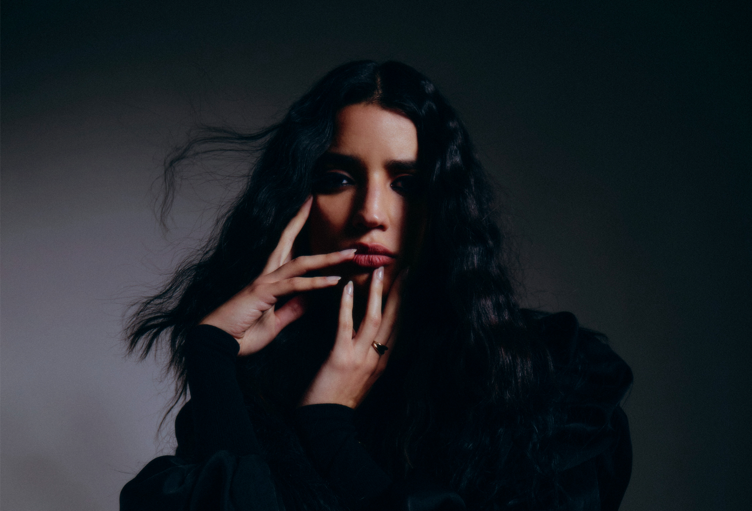 Woman with dark hair in shadowy light, expressive pose, captivating and mysterious.
