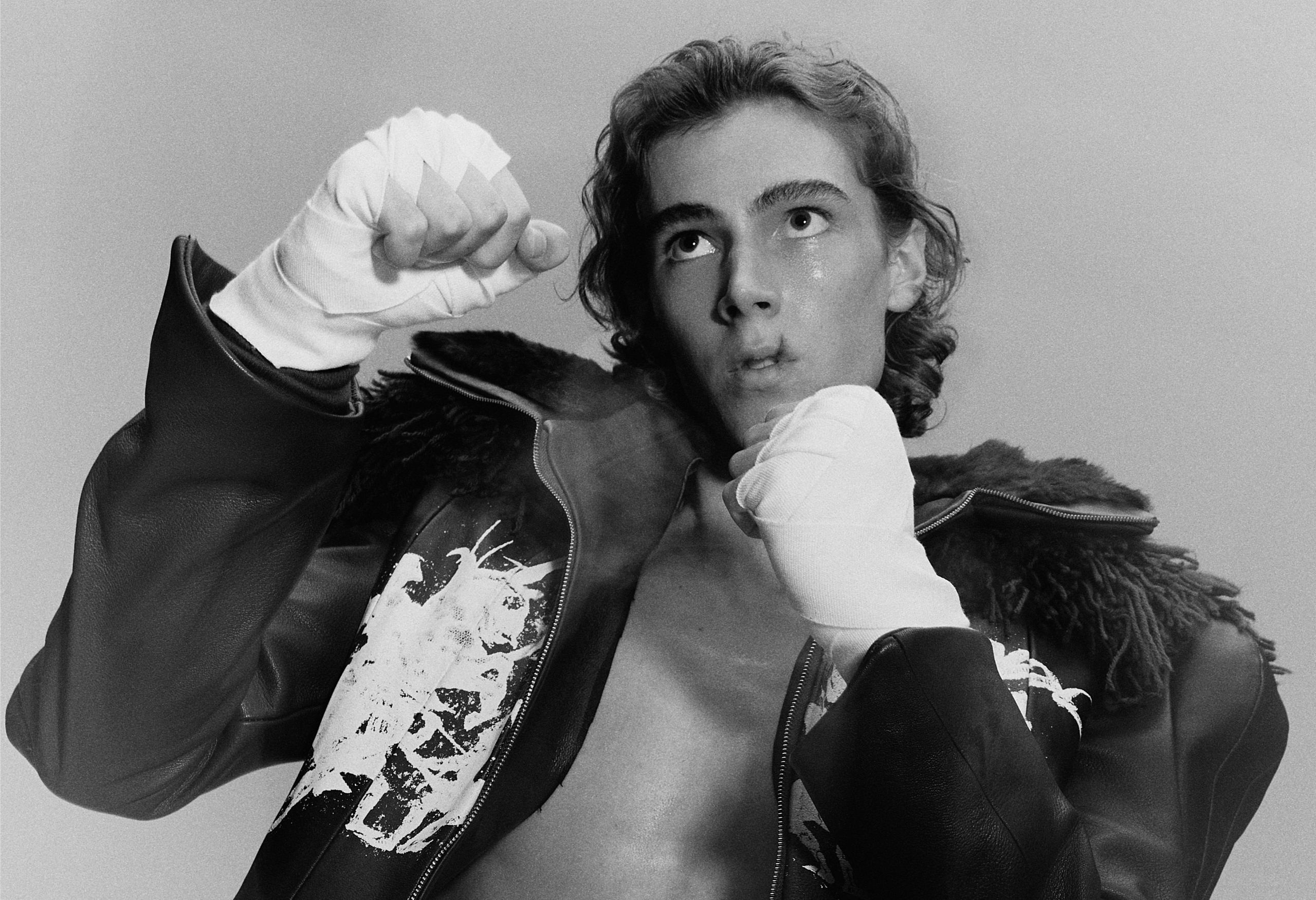 Young boxer in action pose, wearing leather jacket and hand wraps.