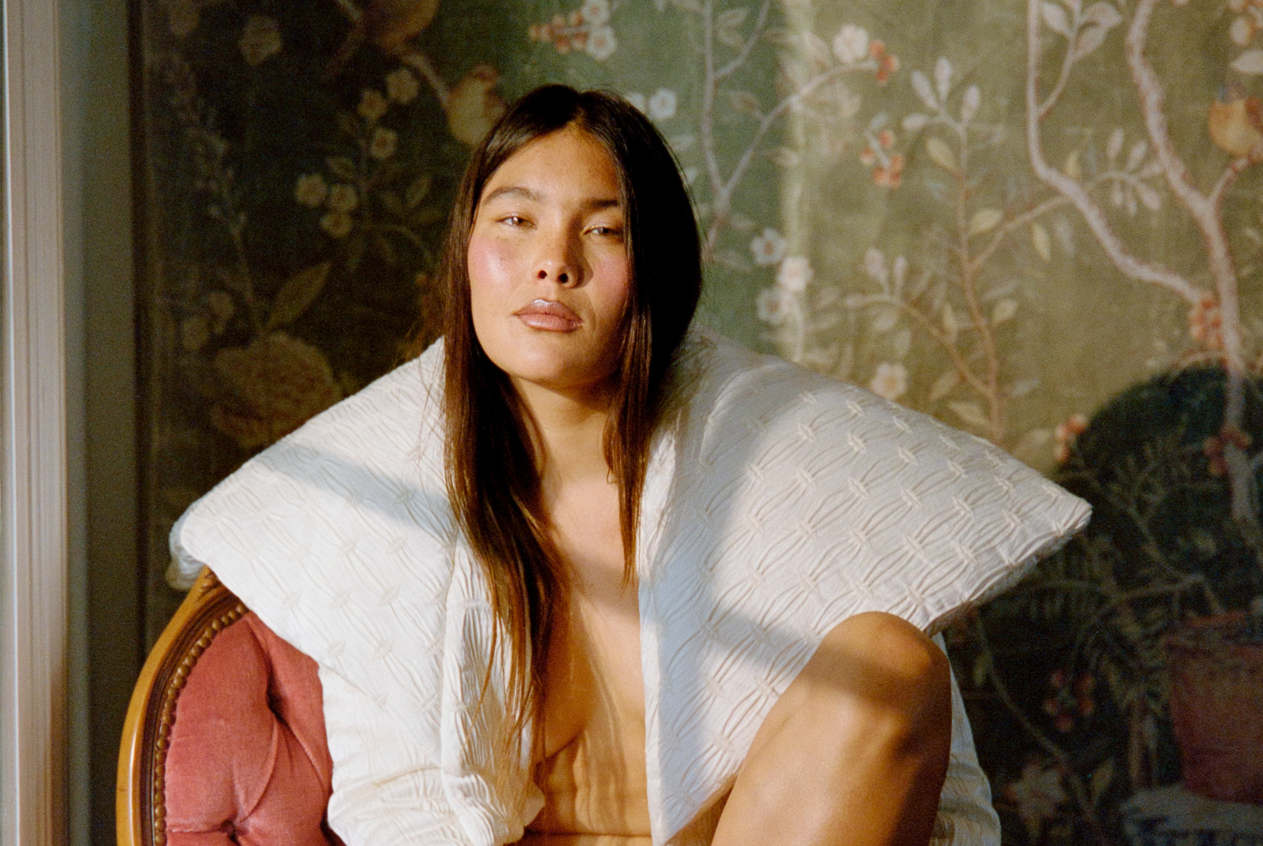 Person in white quilted robe sitting against a floral backdrop.