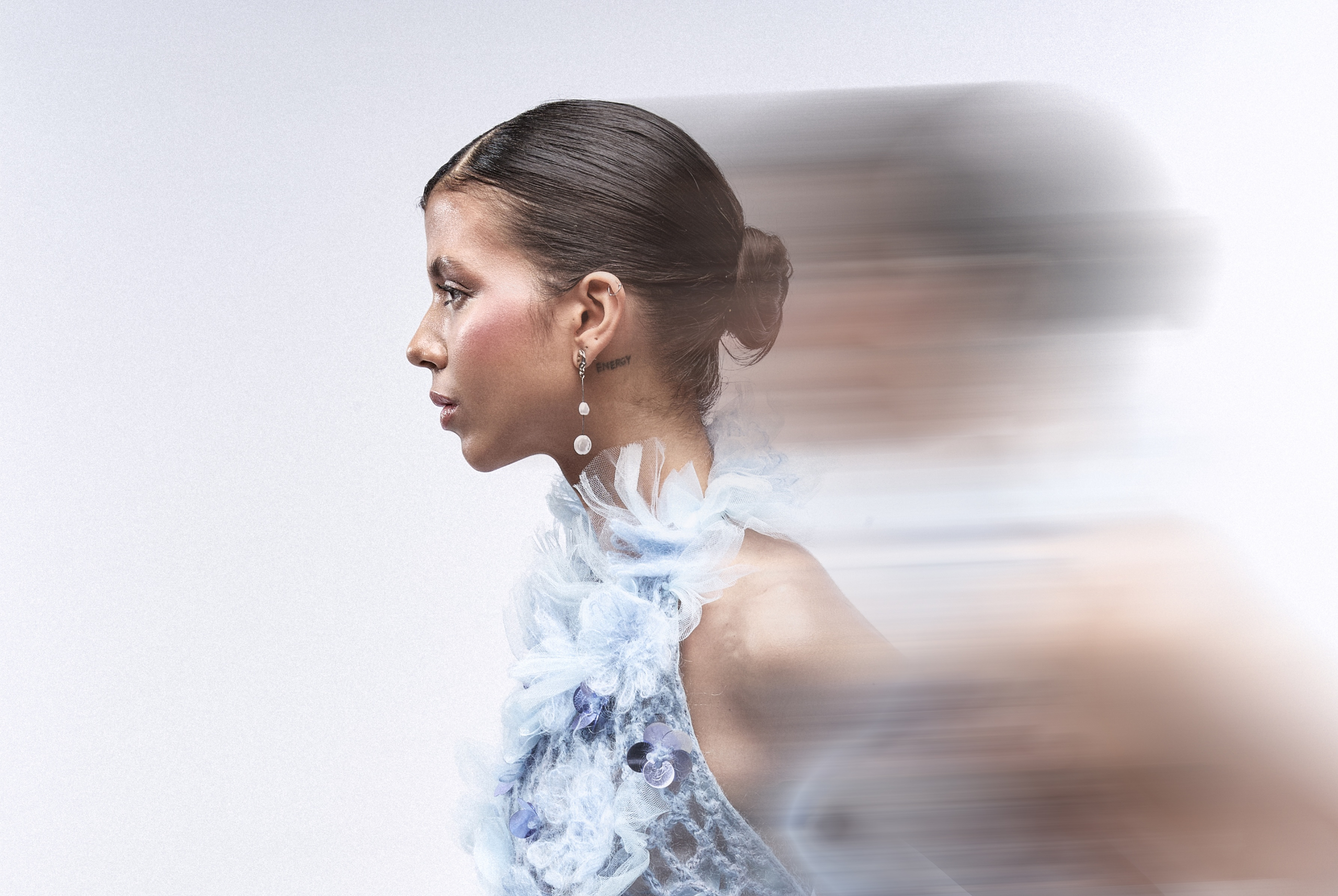 Elegant woman in motion, styled in sheer blue feathers and delicate jewelry.