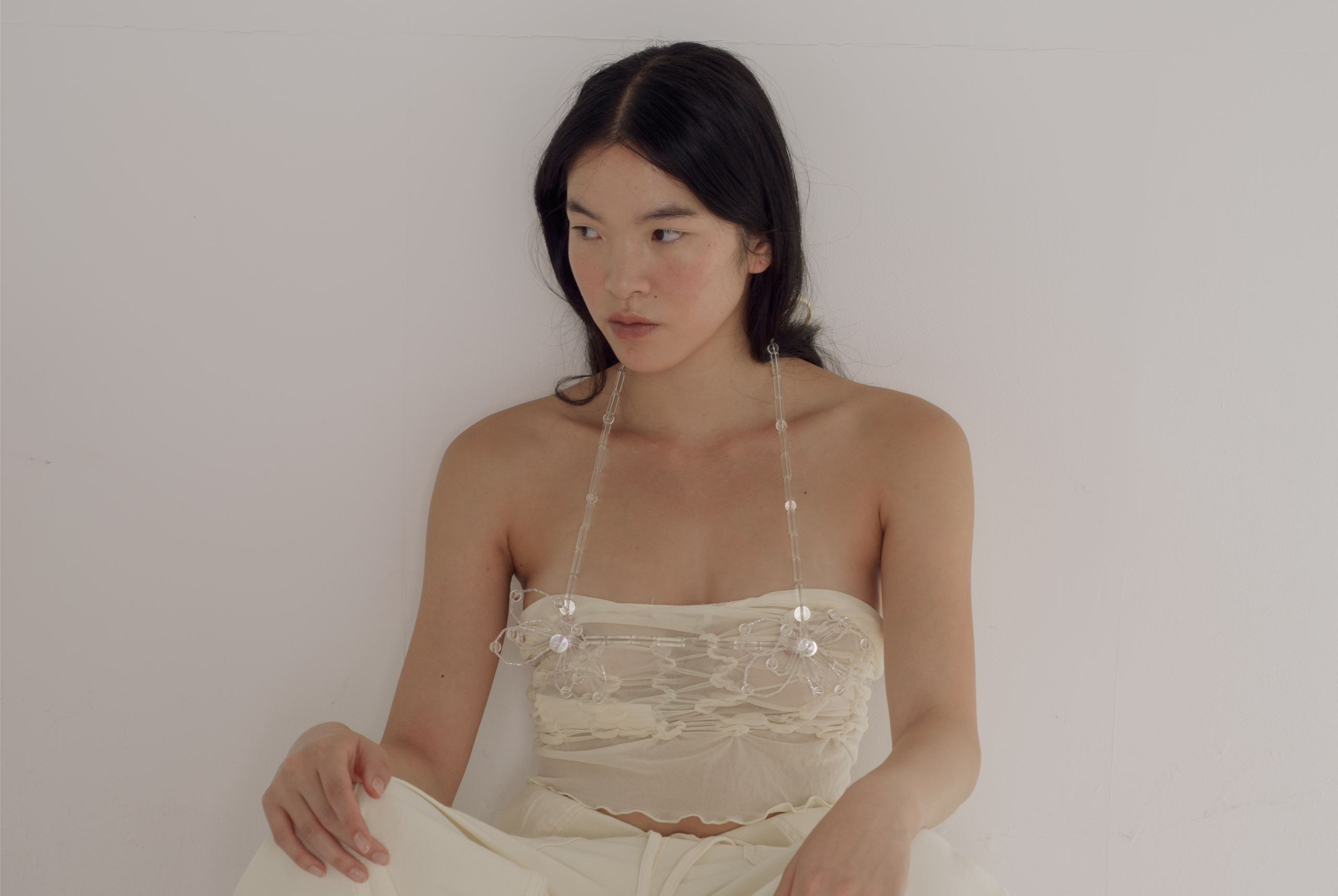 Woman in elegant white top, gazing sideways against a minimalist white backdrop.