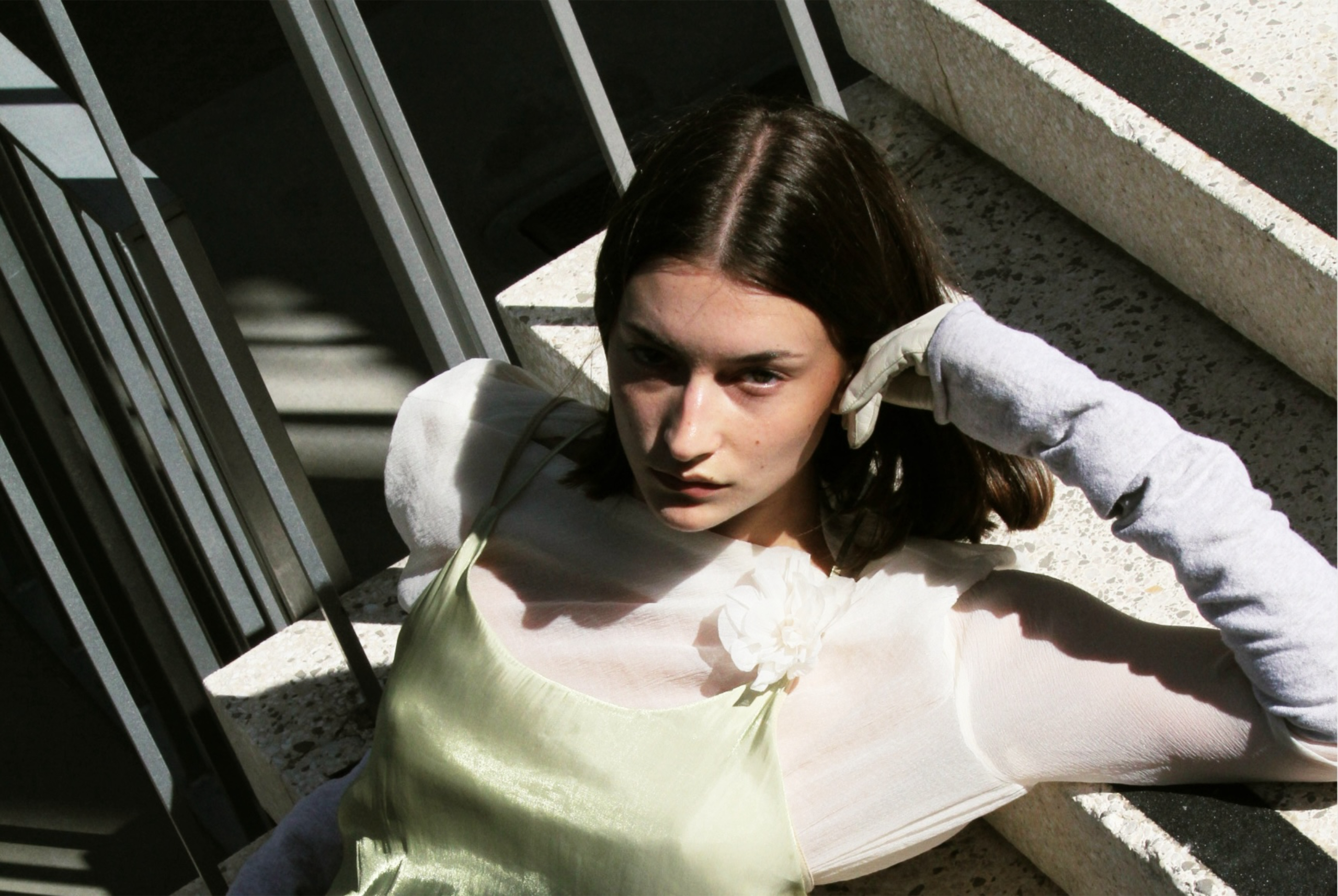 Woman in a green dress and gloves lounging on steps in sunlit setting.