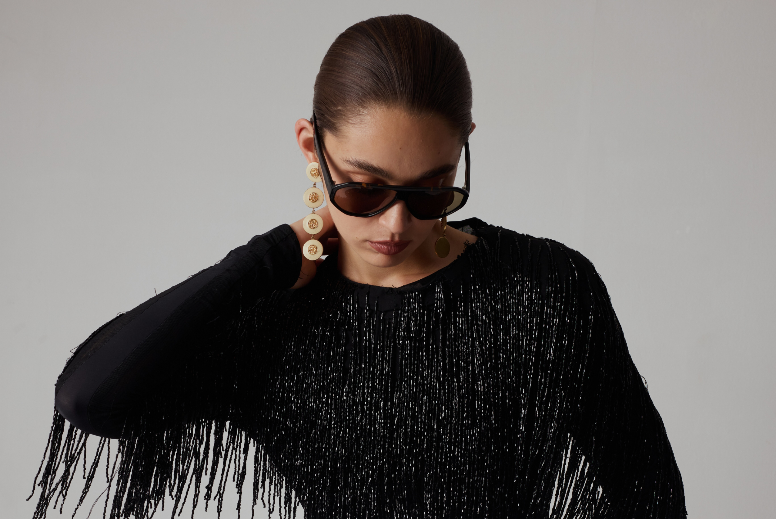 Elegant woman in black fringe dress, sunglasses, and statement earrings.