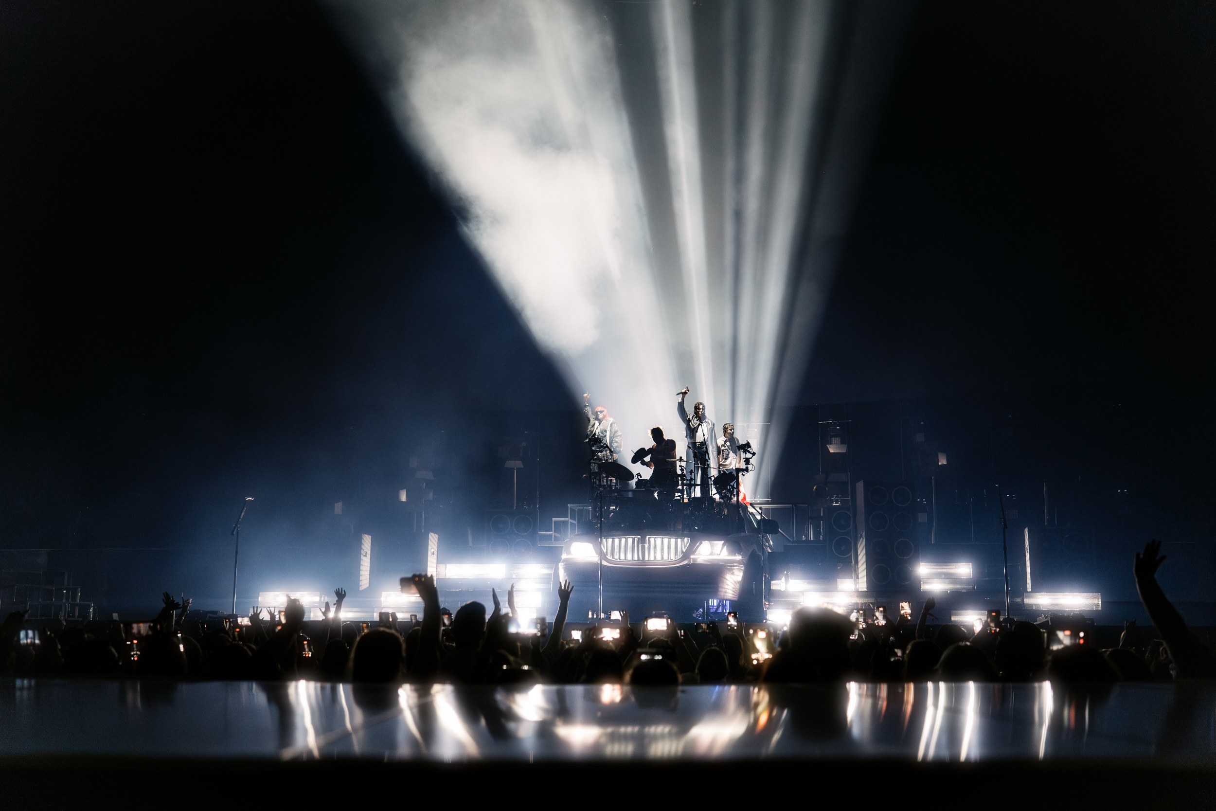 Live concert with dramatic lighting, band performing on stage, crowd cheering.