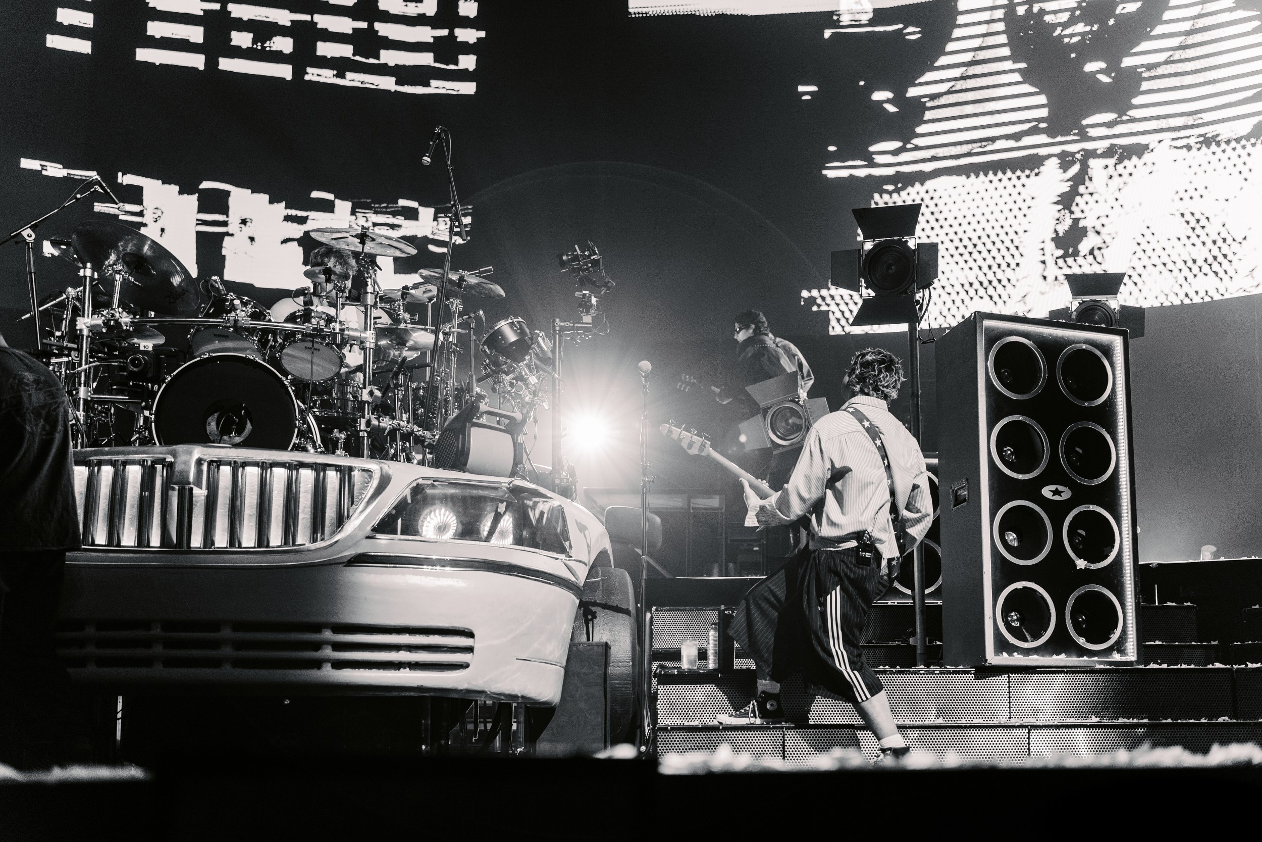 Live rock music performance with bass guitarist and drum set.