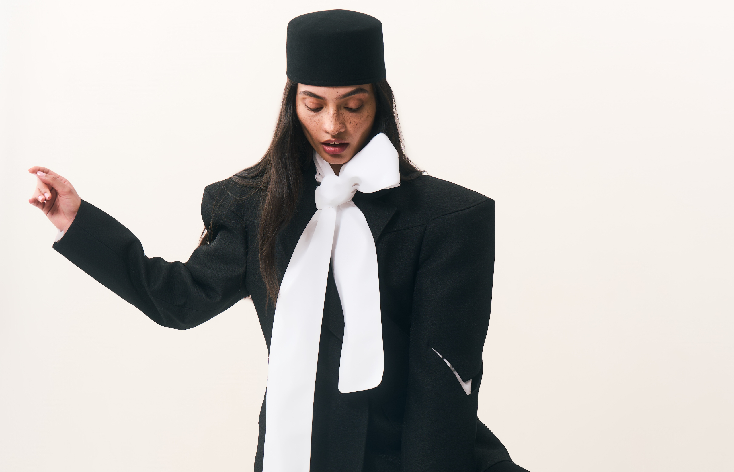 Model in stylish black outfit and white bow tie on a plain background.