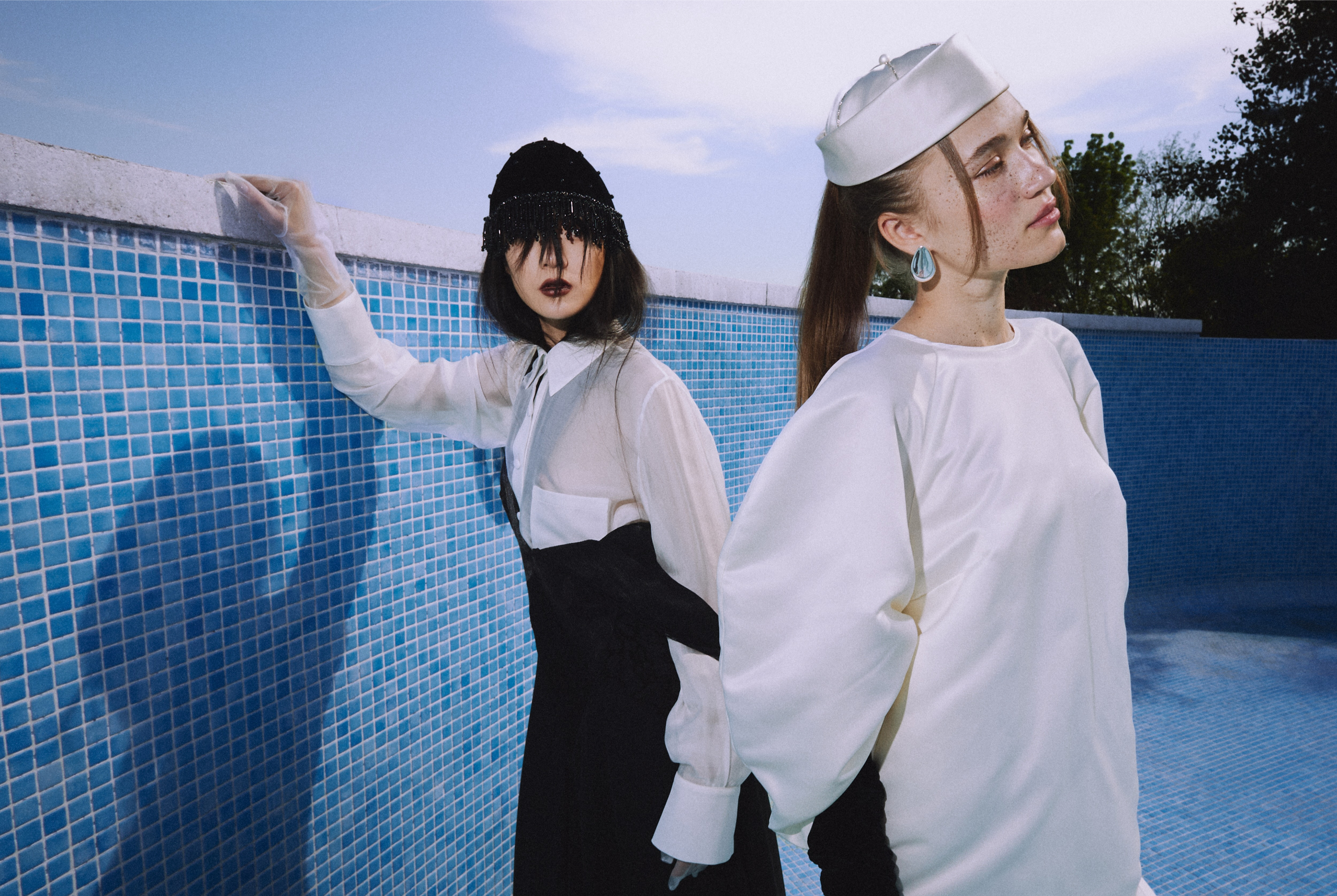 Fashionable women in stylish outfits by a blue-tiled pool backdrop.