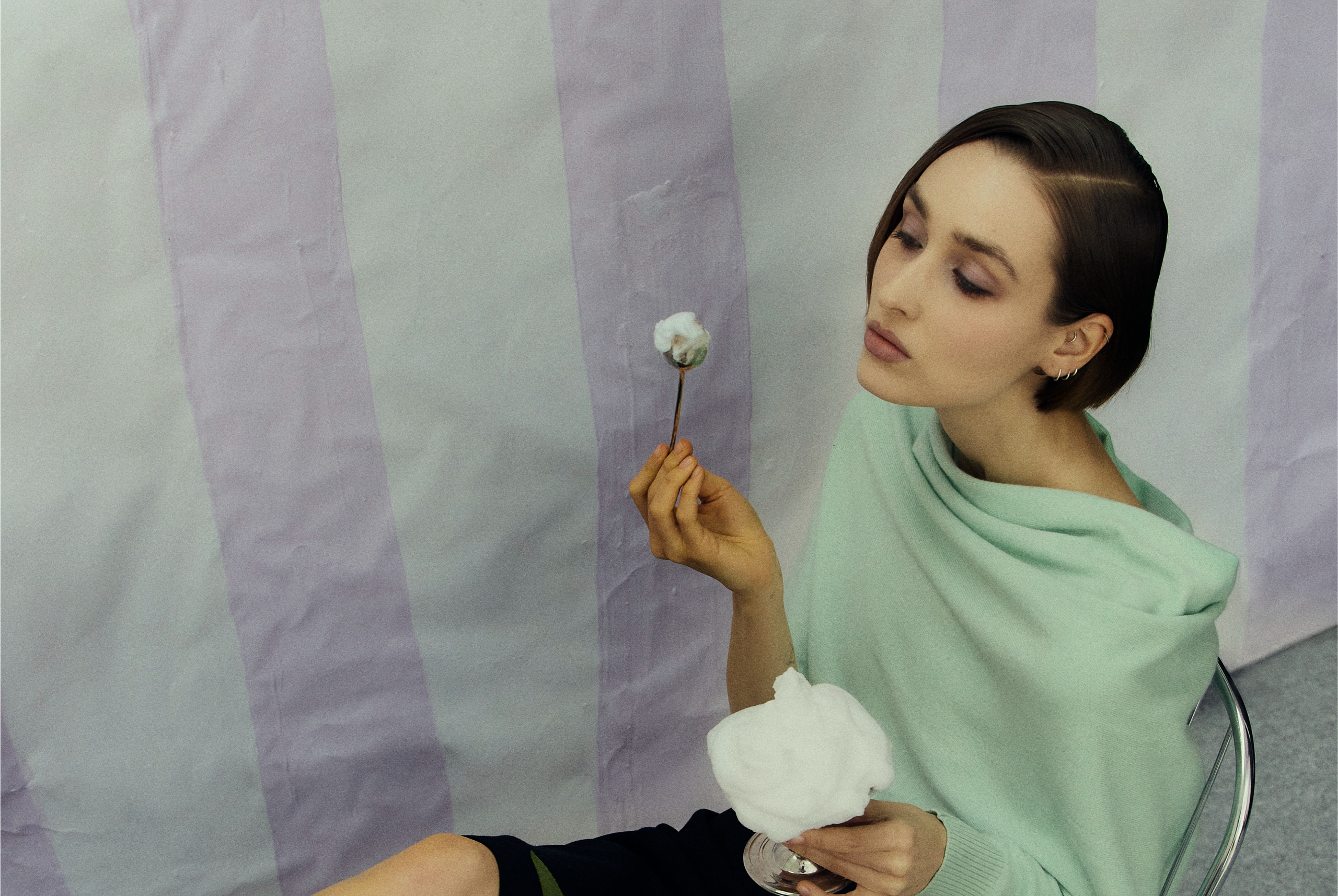 Woman in mint top holding cotton candy with pastel striped background.