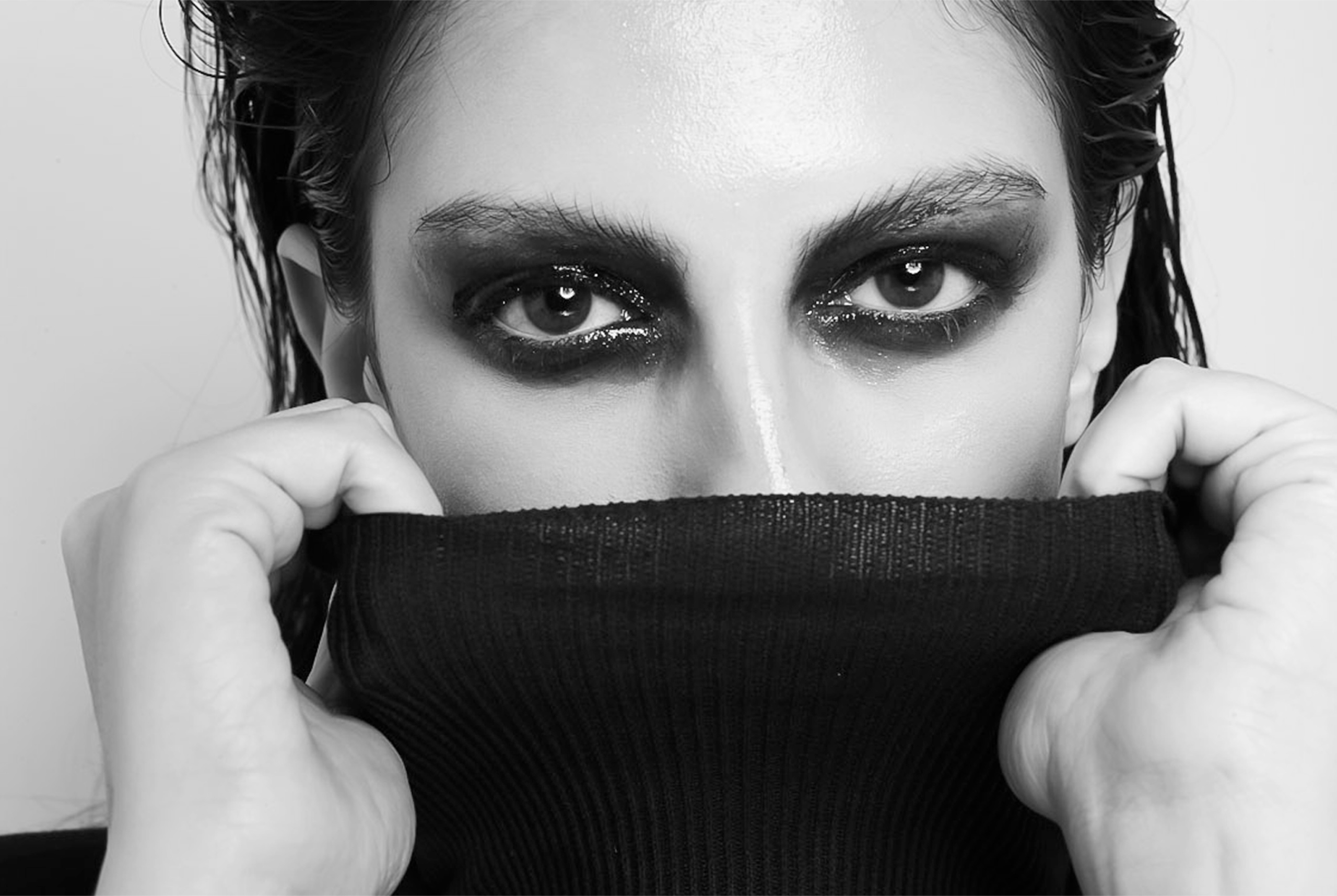 Close-up of person with bold eye makeup, covering face with a black turtleneck.