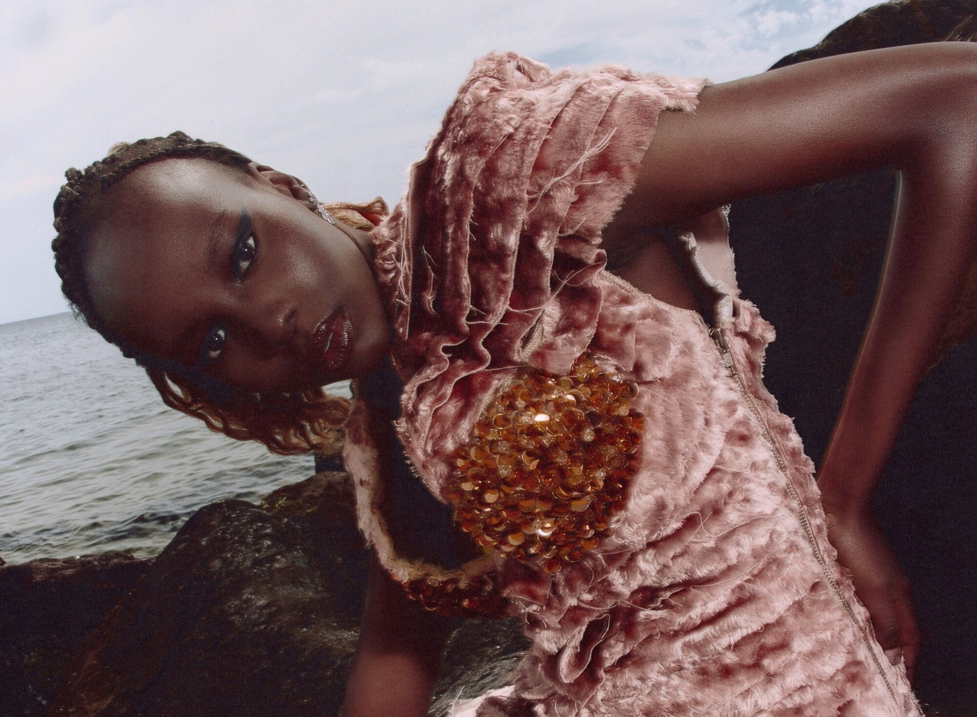 Model in pink textured dress by the sea.