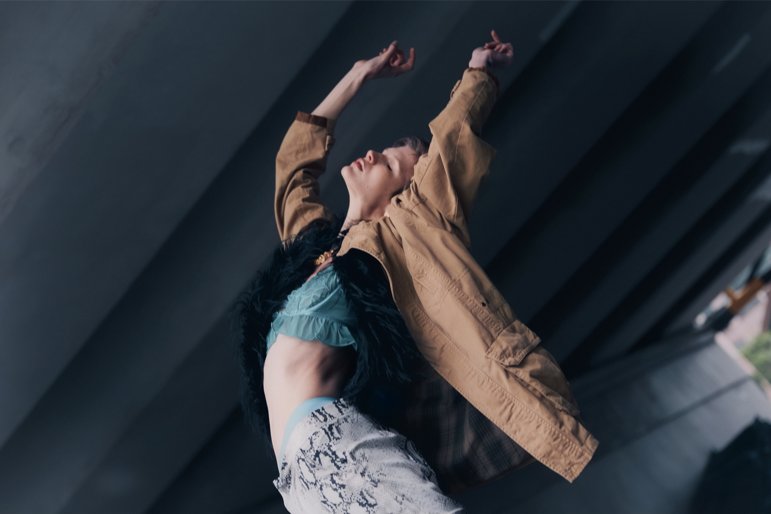 Person dancing expressively in stylish outfit under bridge.
