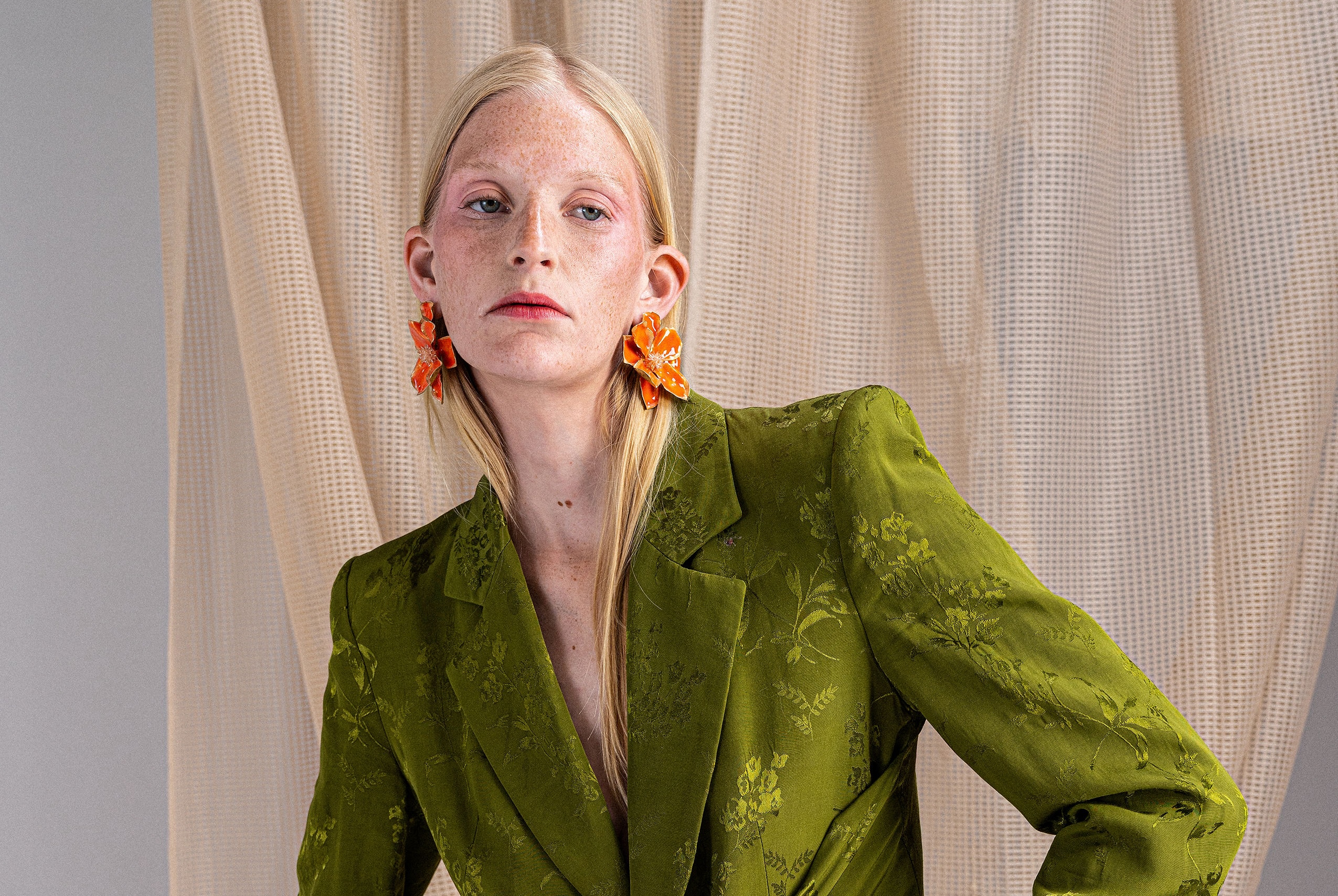 Model in green floral blazer with orange flower earrings. Fashion portrait.