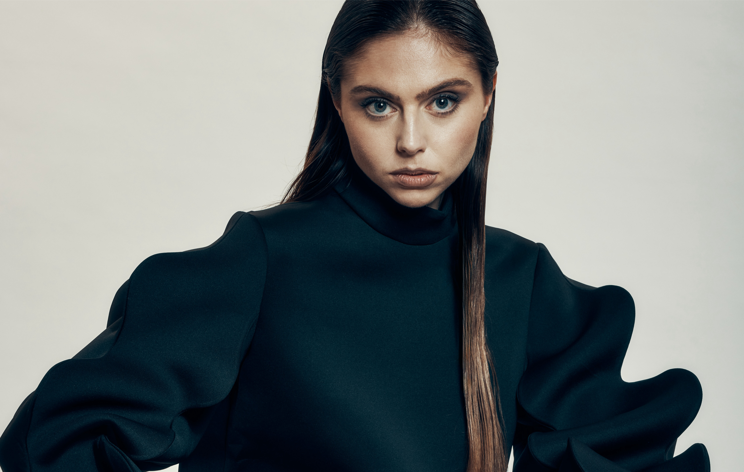 Fashion portrait of a woman in a dramatic black top, looking directly at the camera.
