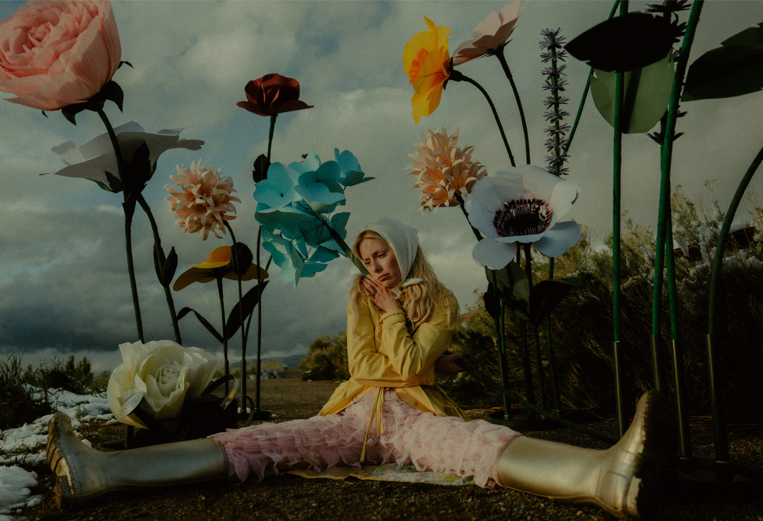Person in yellow jacket among giant colorful flowers, wearing gold boots.