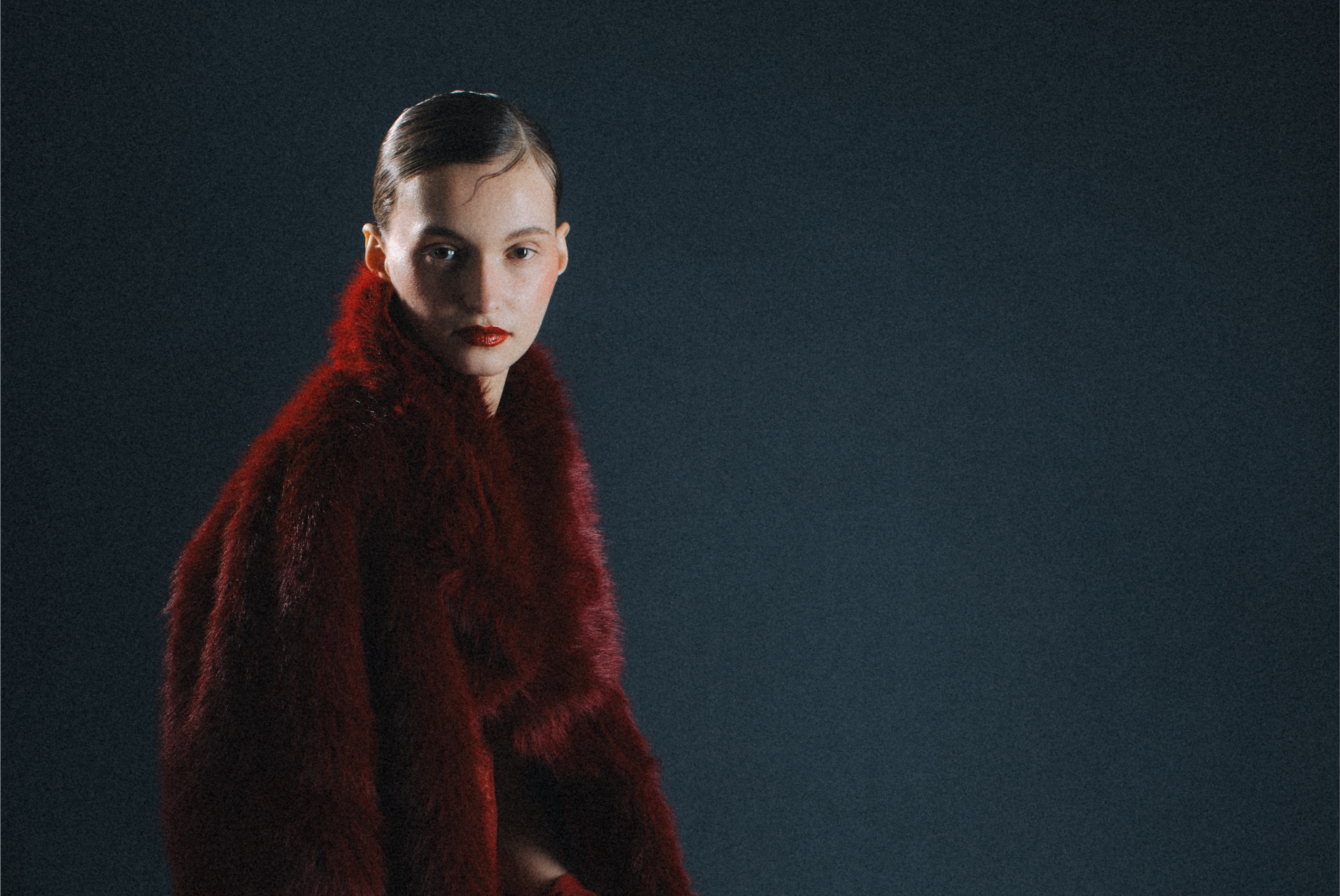 Elegant model in a red fur coat against a dark backdrop.