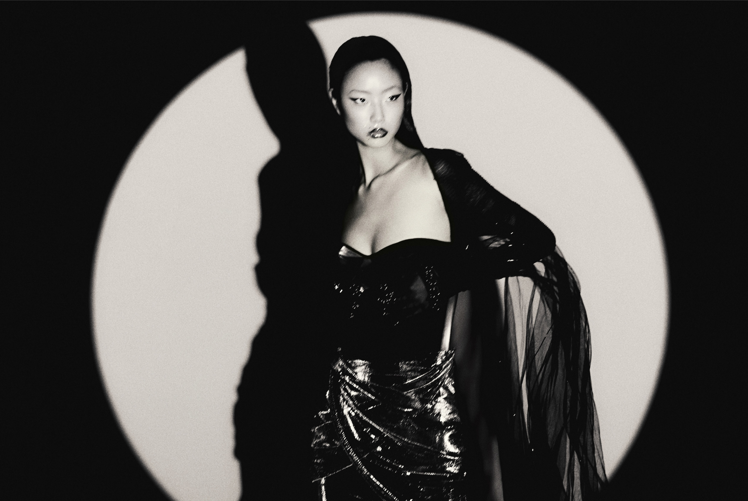 Elegant woman in dramatic black dress, bold lighting, high fashion portrait.