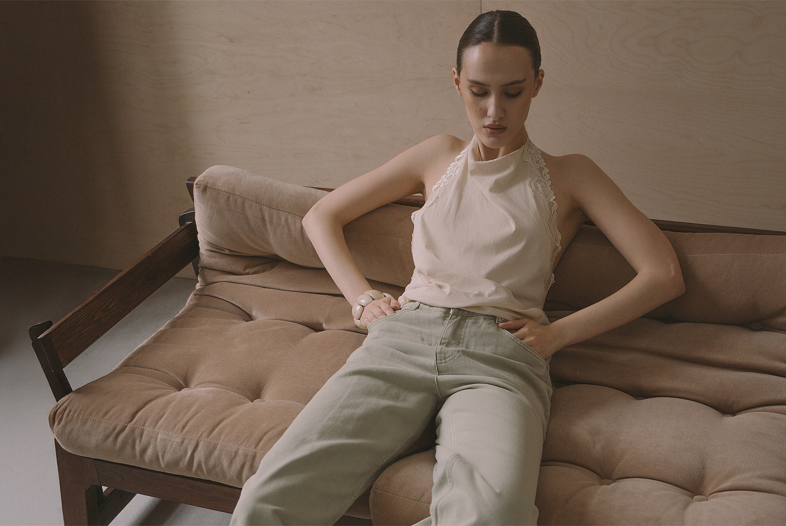 Woman in casual outfit sitting on a beige sofa in a minimalist room.