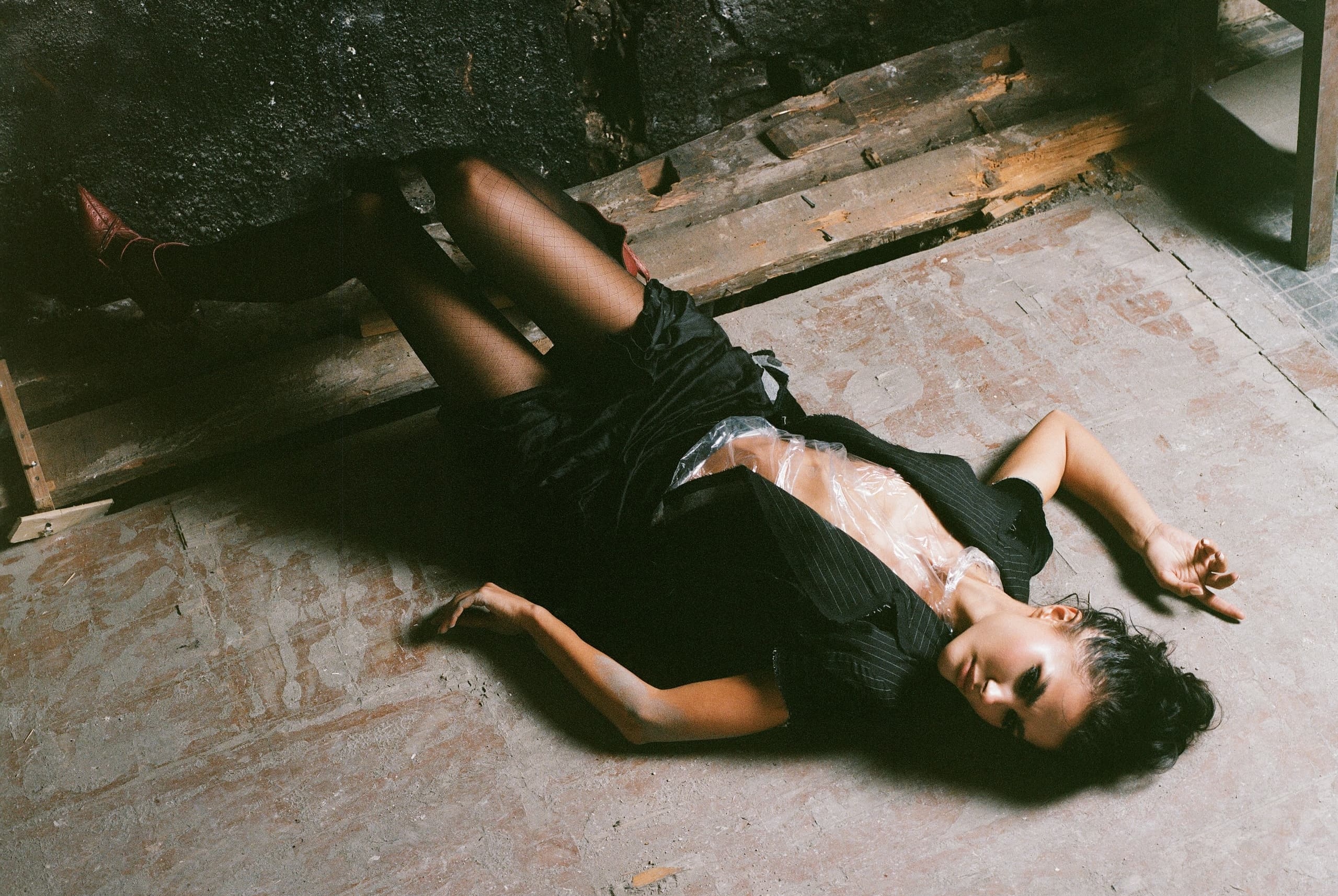 Person lying on a rustic floor in artistic black attire, creative fashion photo.