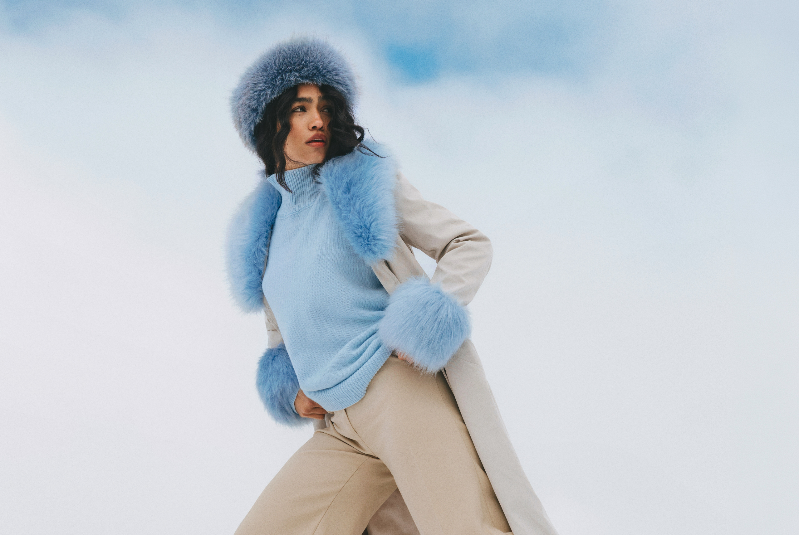 Woman in stylish blue fur-trimmed coat against snowy backdrop.