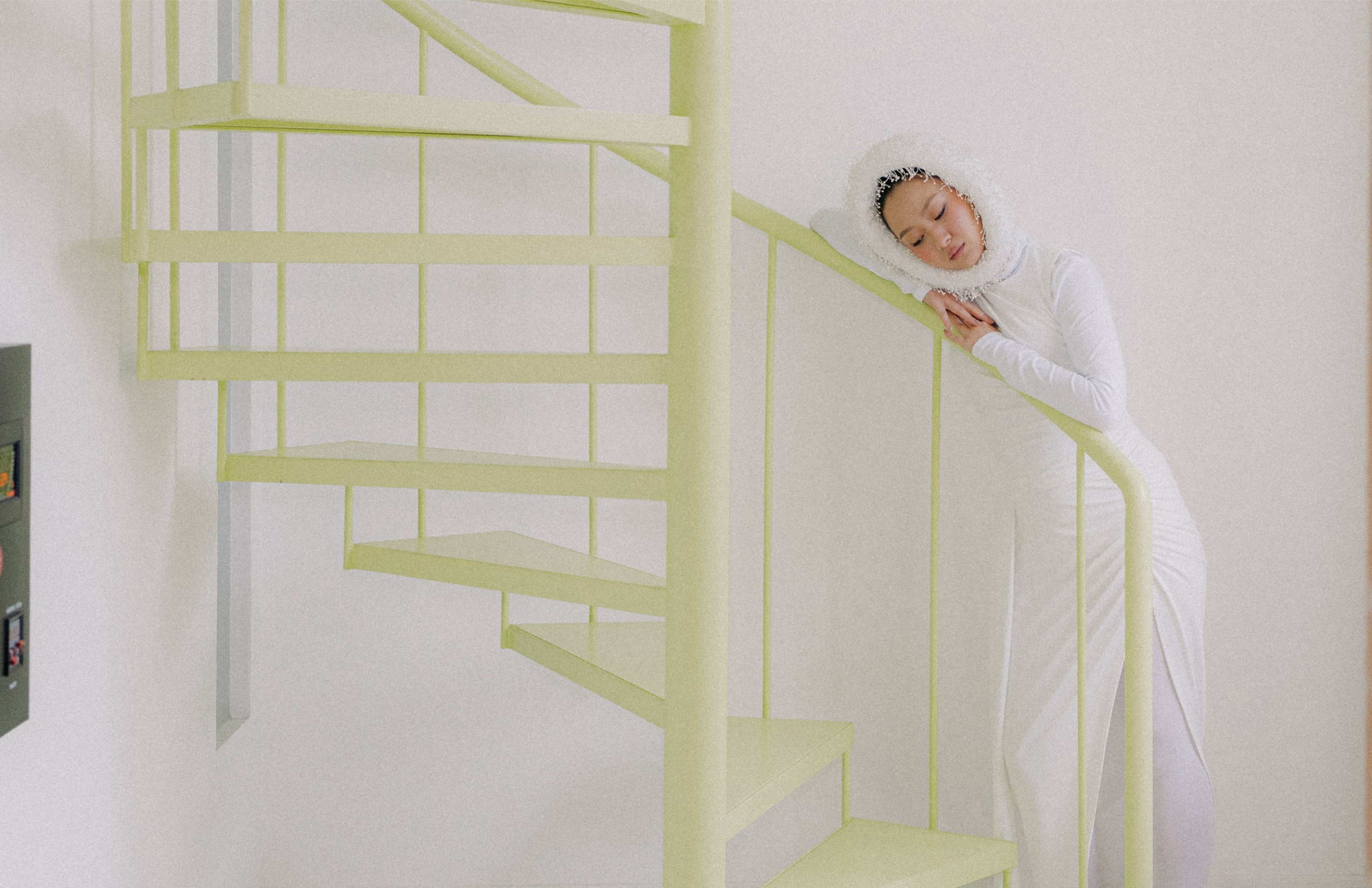 Woman in white dress resting on spiral staircase, serene indoor scene.