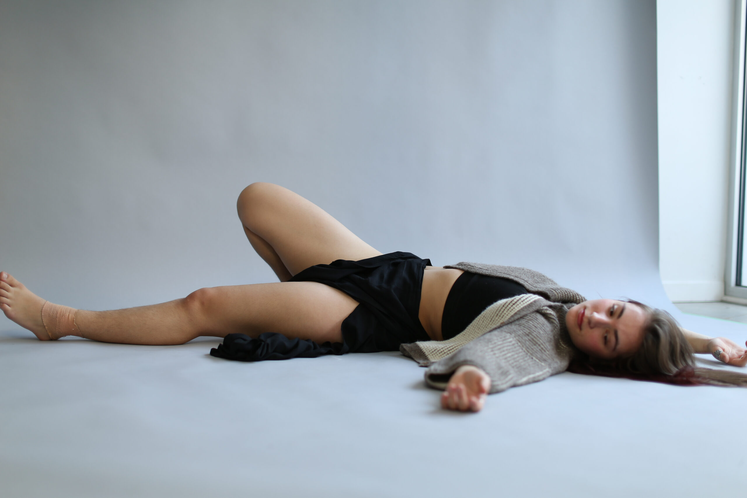 Woman in casual attire lying on the floor, posing for a creative fashion photoshoot.