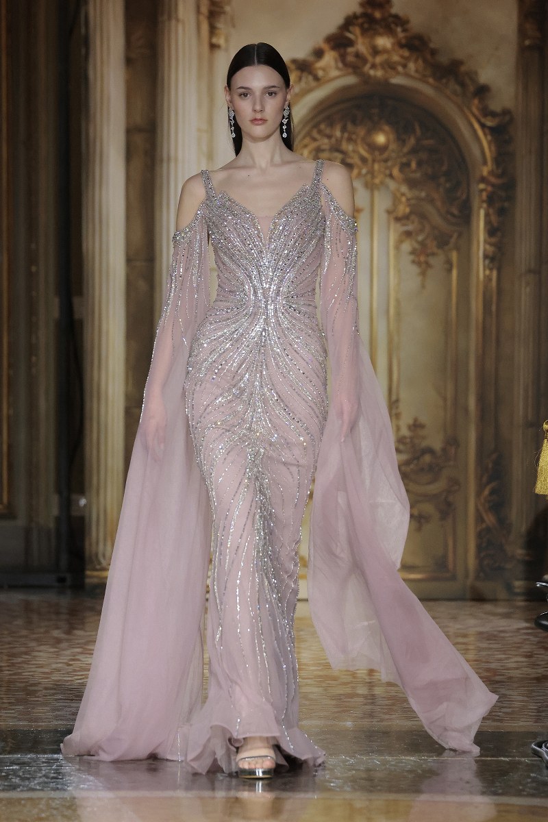 Model in elegant beaded pink gown on runway, fashion show glamour.
