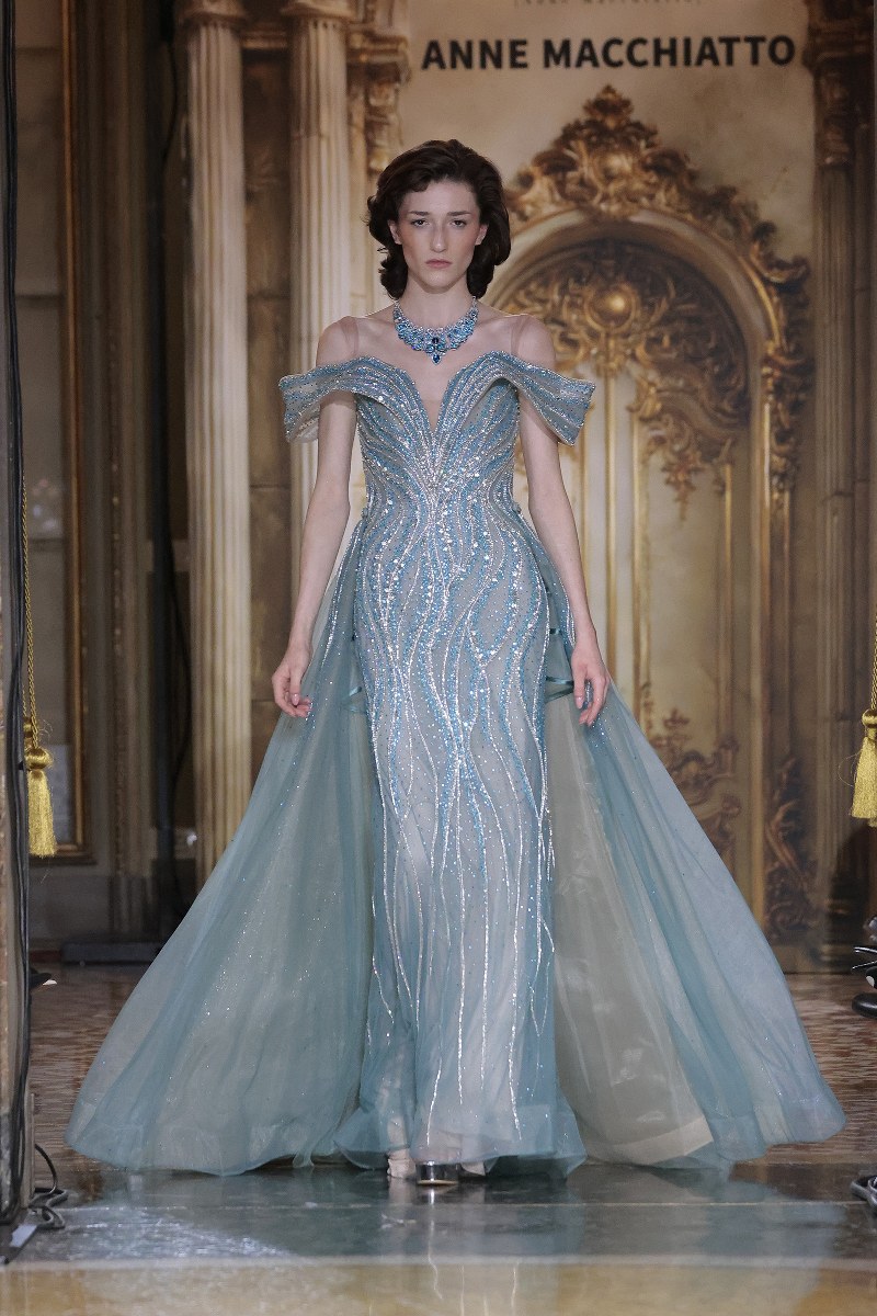 Elegant model in a shimmering blue gown on the runway at a fashion show.