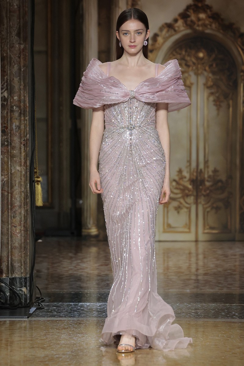 Elegant model in shimmering pink gown on opulent runway.