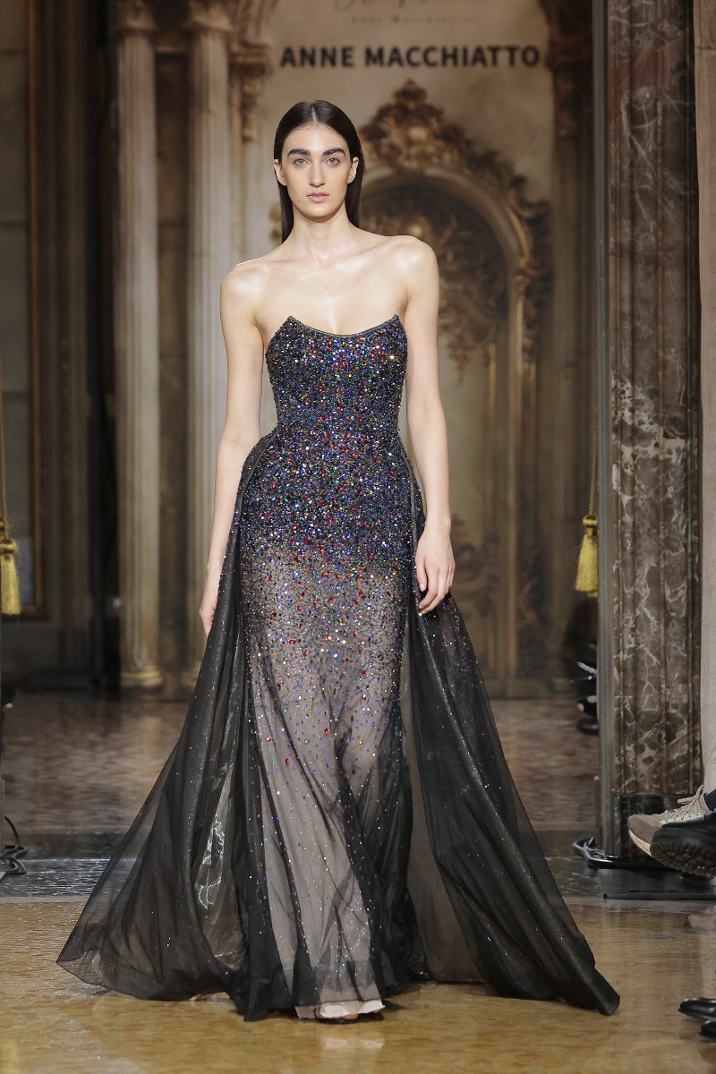 Model in sparkling black evening gown on runway.