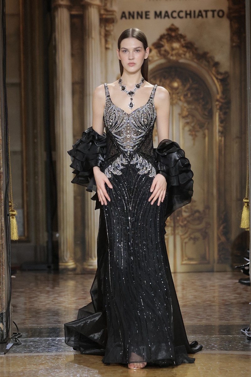 Model walking in an elegant black gown at a fashion show.