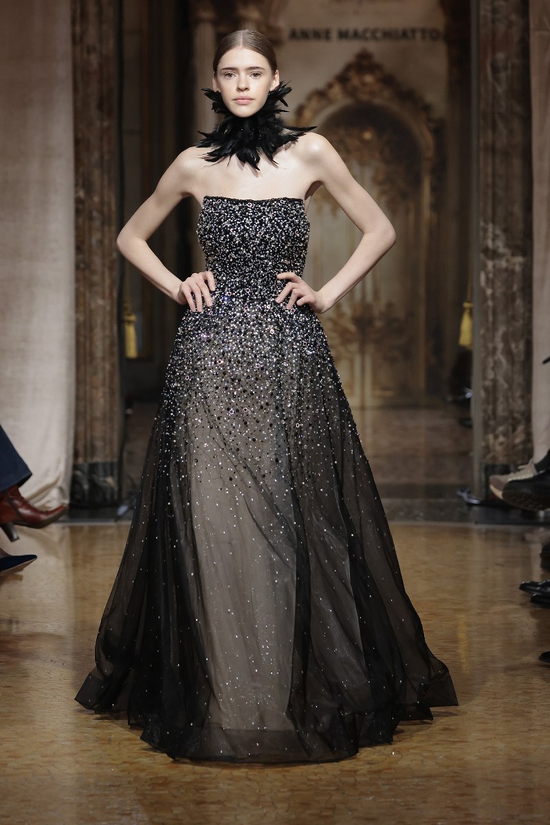 Model in sparkling black gown on runway, fashion show elegance.