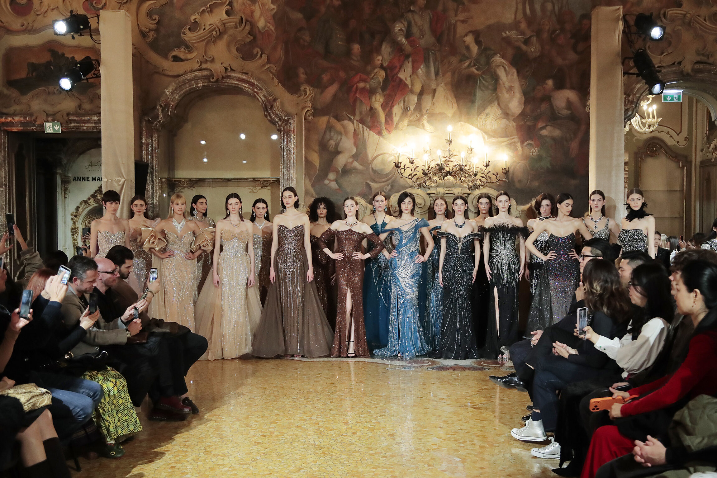 Elegant fashion show models in stunning gowns on a grand runway.