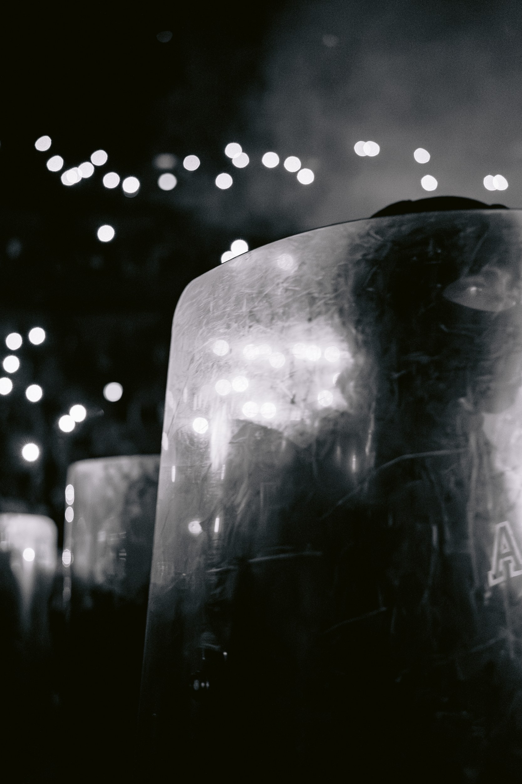 Police shield in a dark, smoky night, illuminated by scattered city lights.