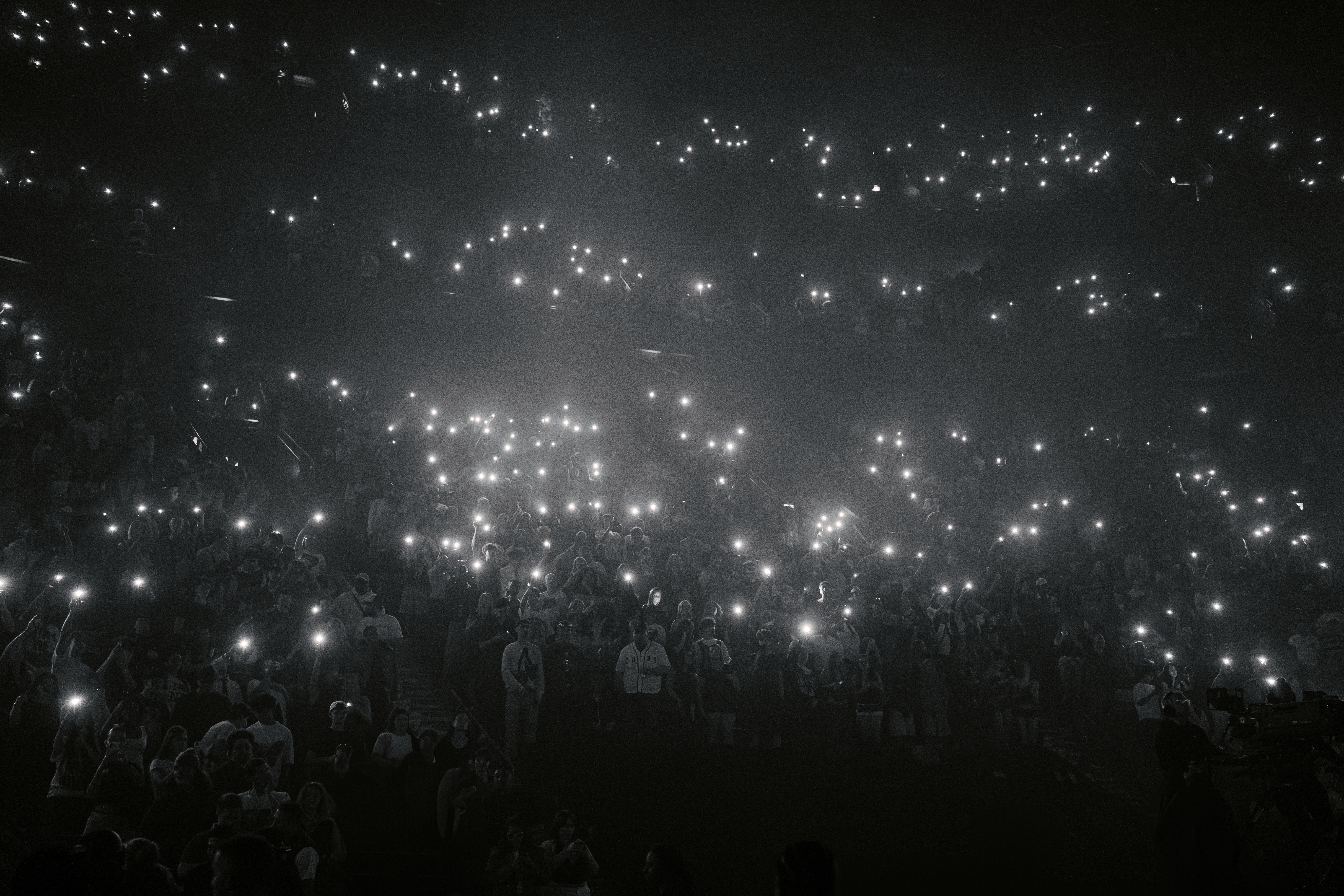 Concert crowd with glowing phone lights in a dark stadium.