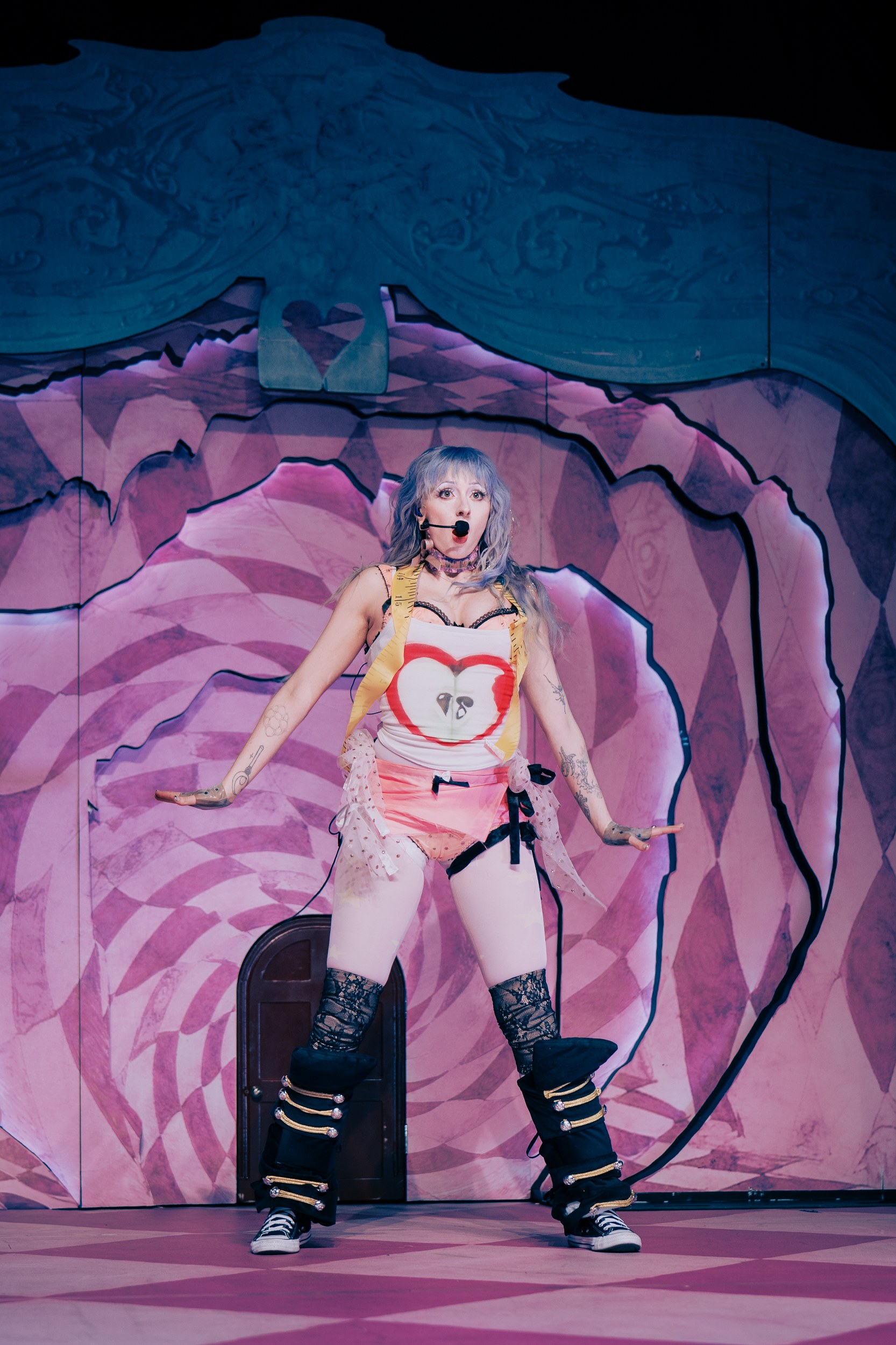 Performer onstage in colorful, eclectic costume with vibrant pink backdrop.
