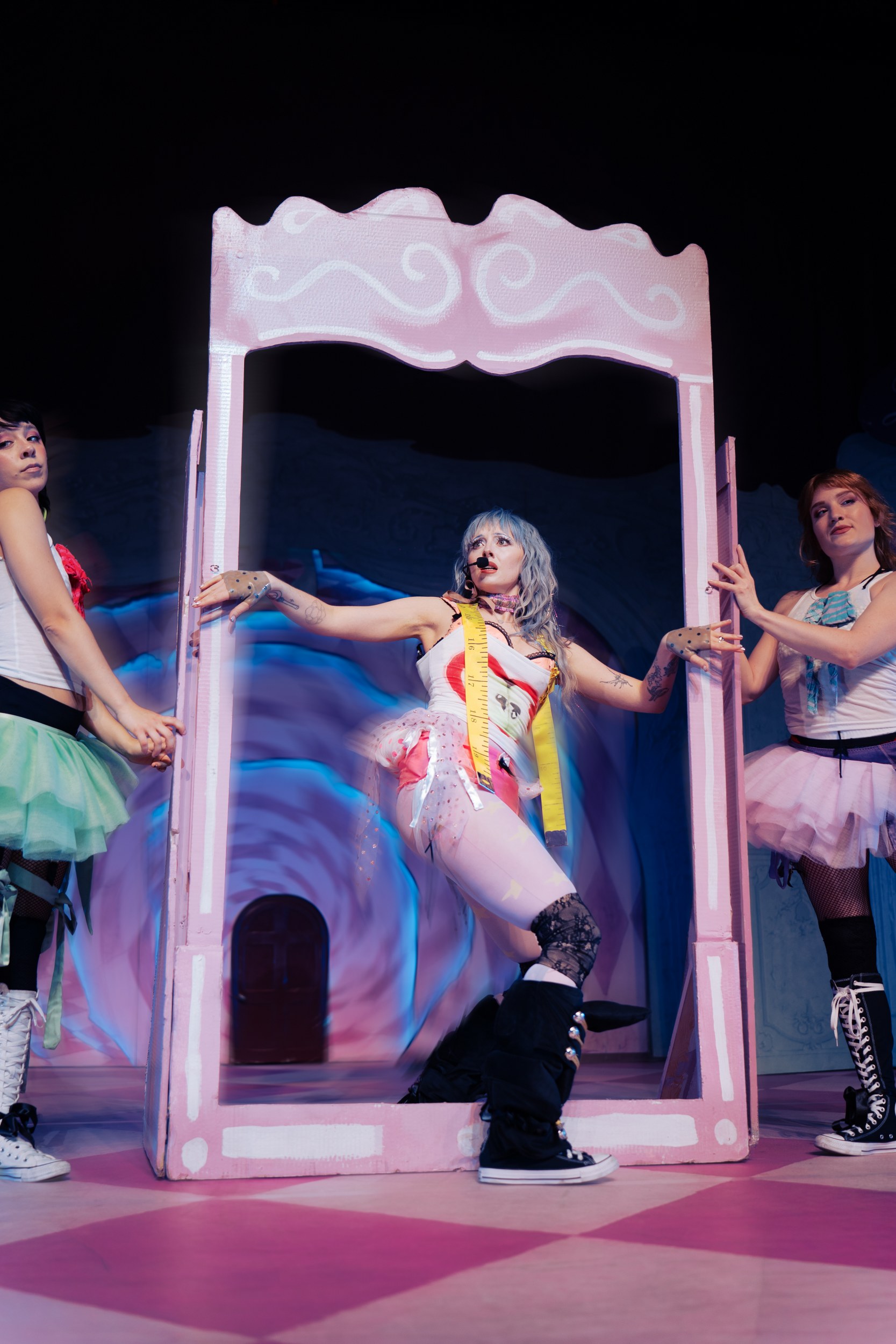 Performers in colorful costumes on stage with pink set design.