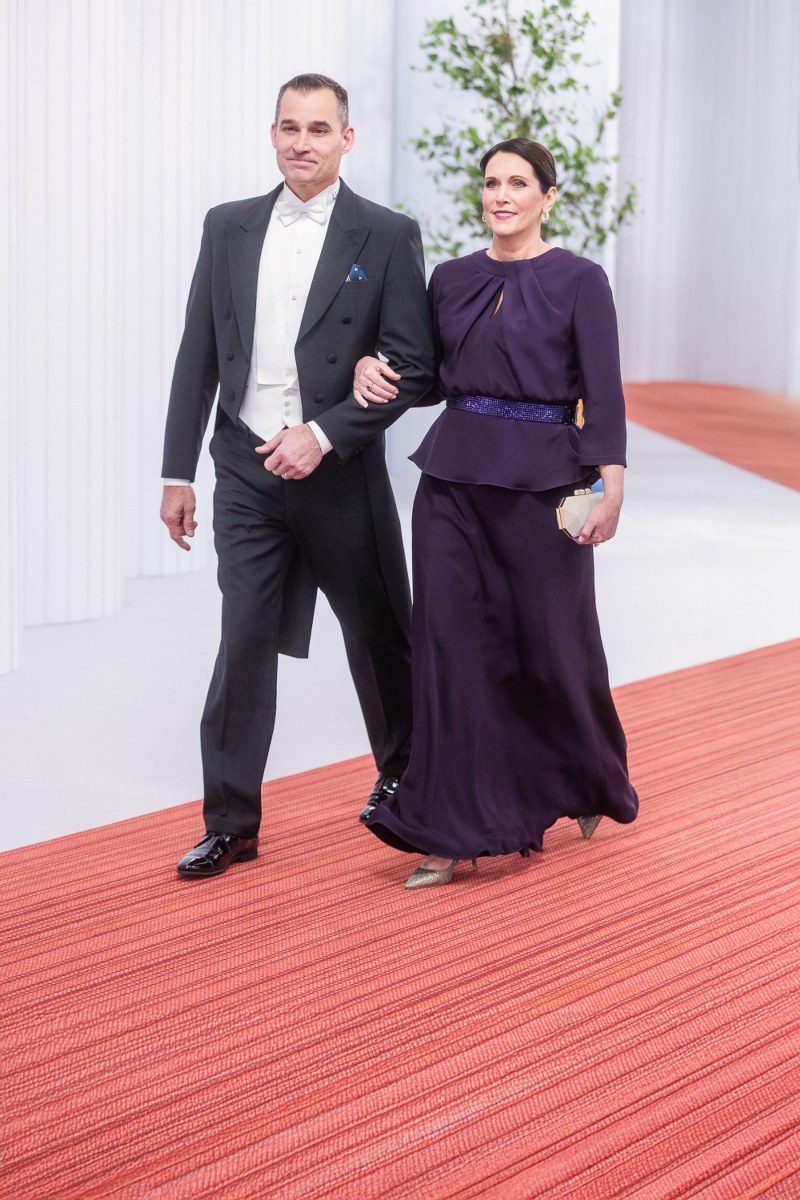 Elegant couple walking on red carpet in formal attire at event.