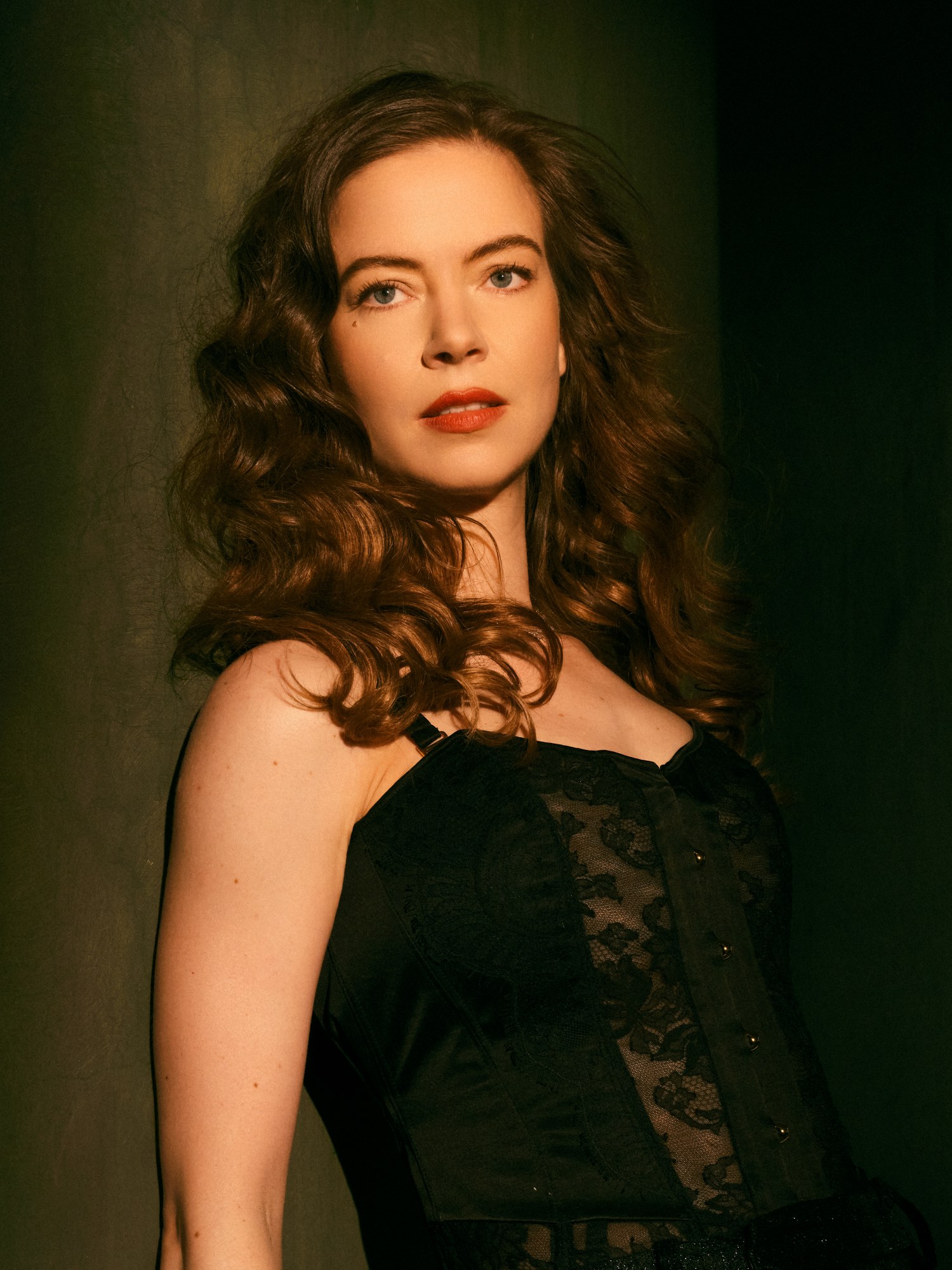 Woman with long wavy hair in elegant black corset, standing confidently.