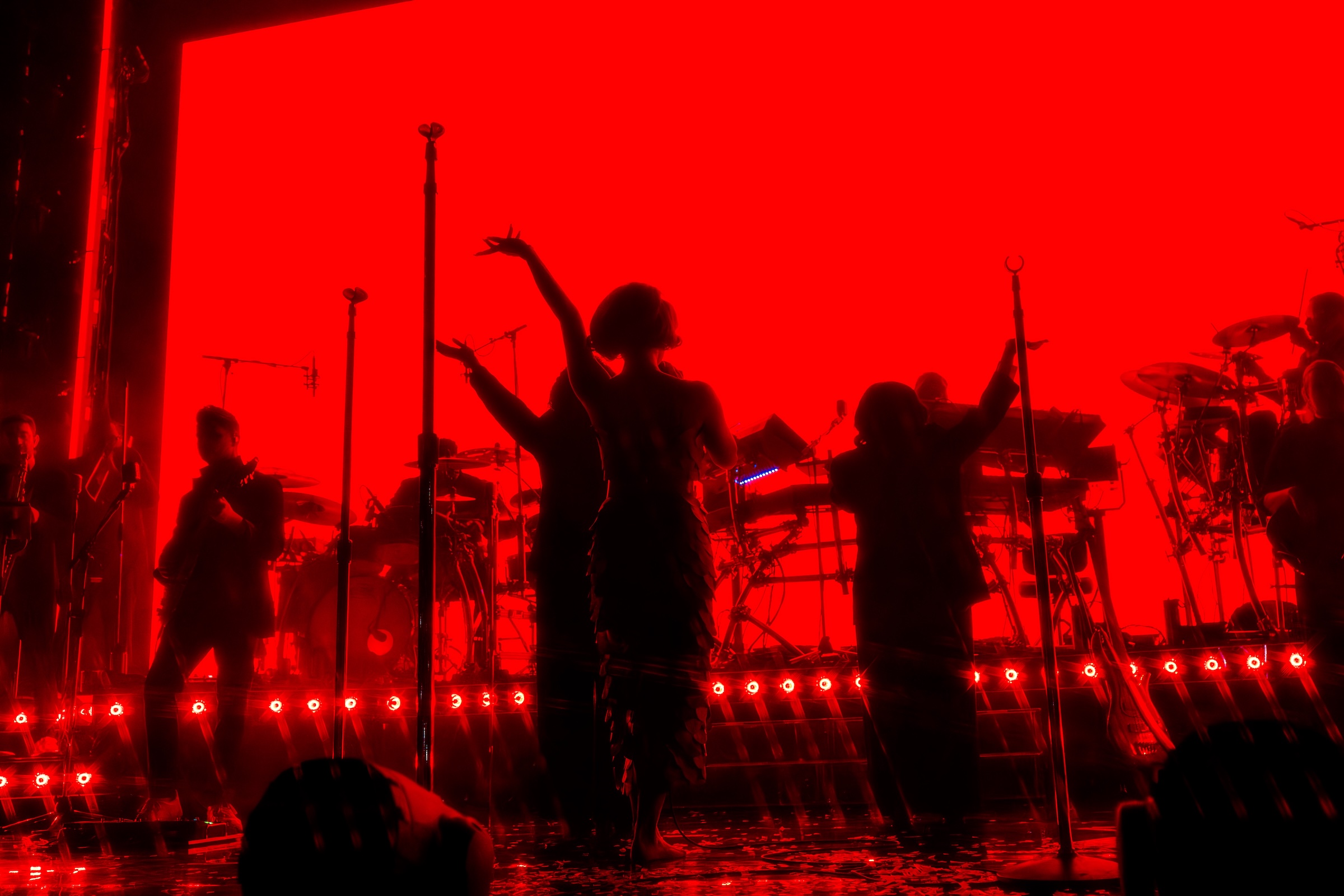 Silhouetted band performing on stage with vibrant red background.