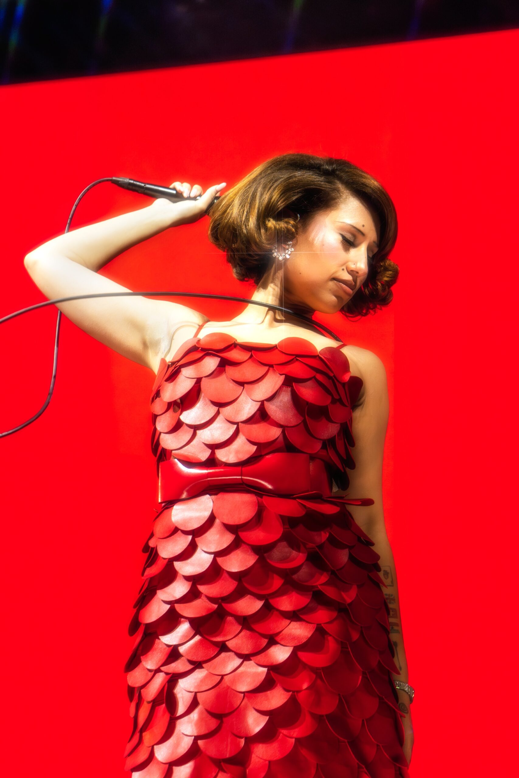 Singer performing in vibrant red dress against bold red background.