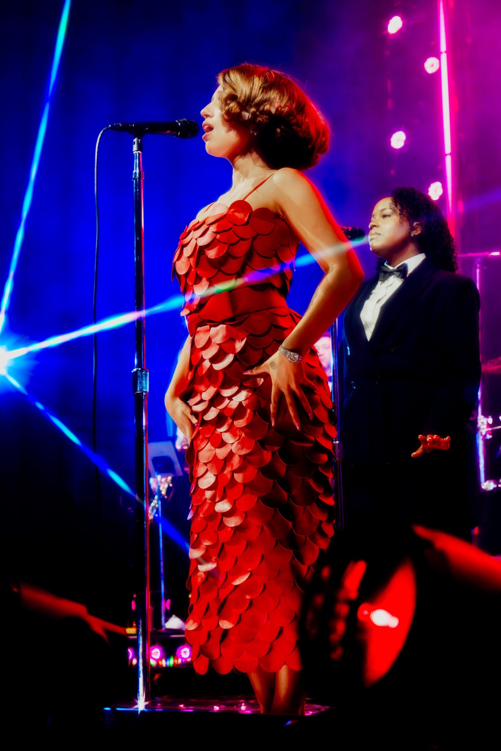 Singer performs onstage in a red dress with vibrant lighting.