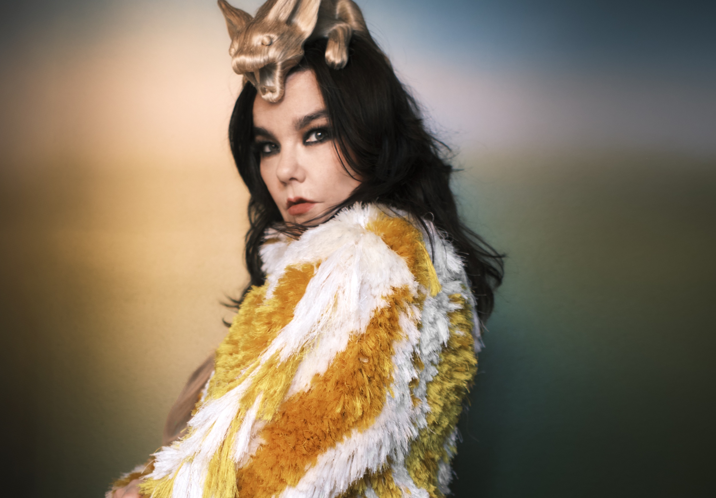 Woman in colorful fur outfit with artistic headpiece against blurred background.