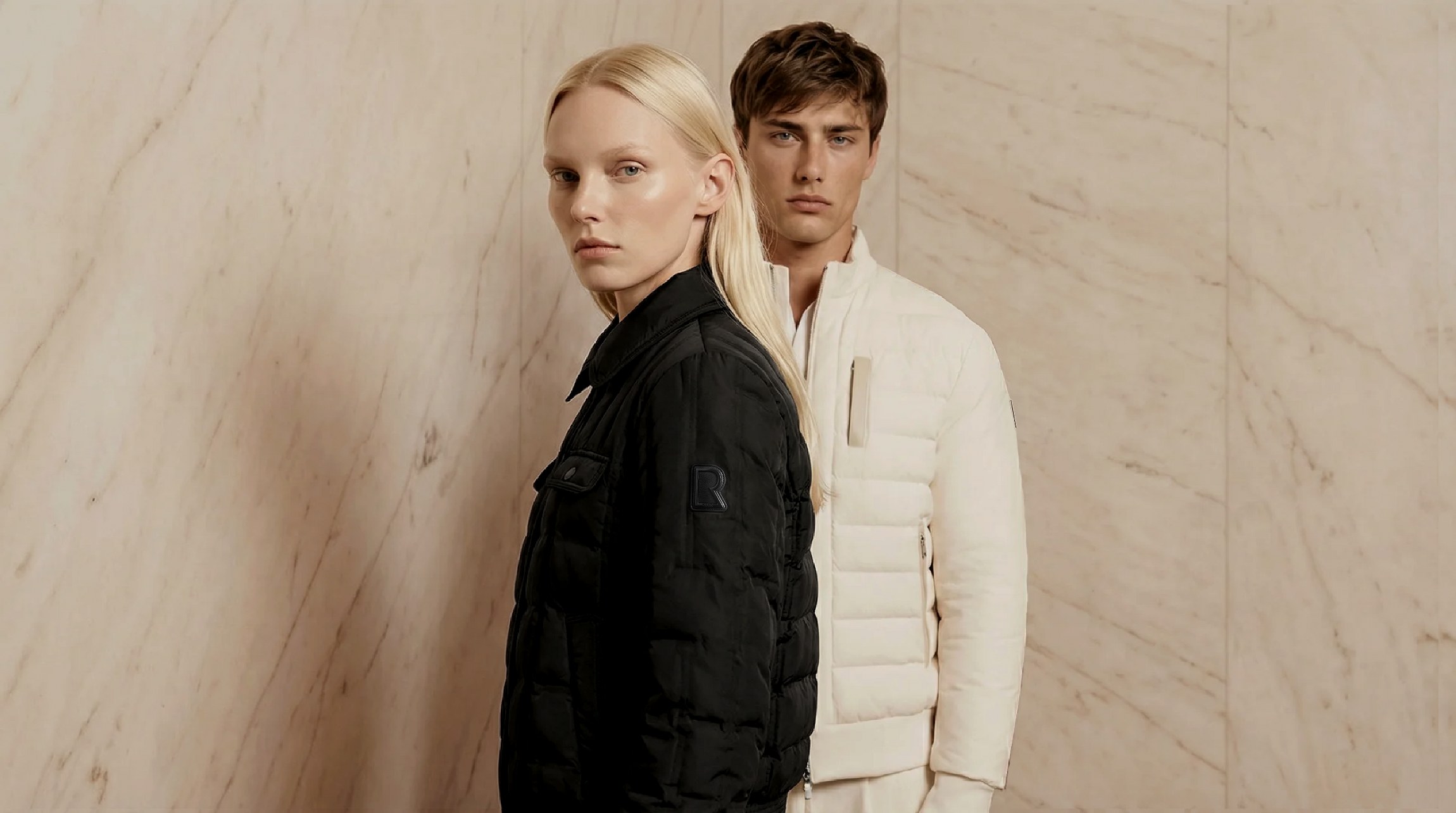 Fashionable couple in stylish black and white jackets against a marble backdrop.