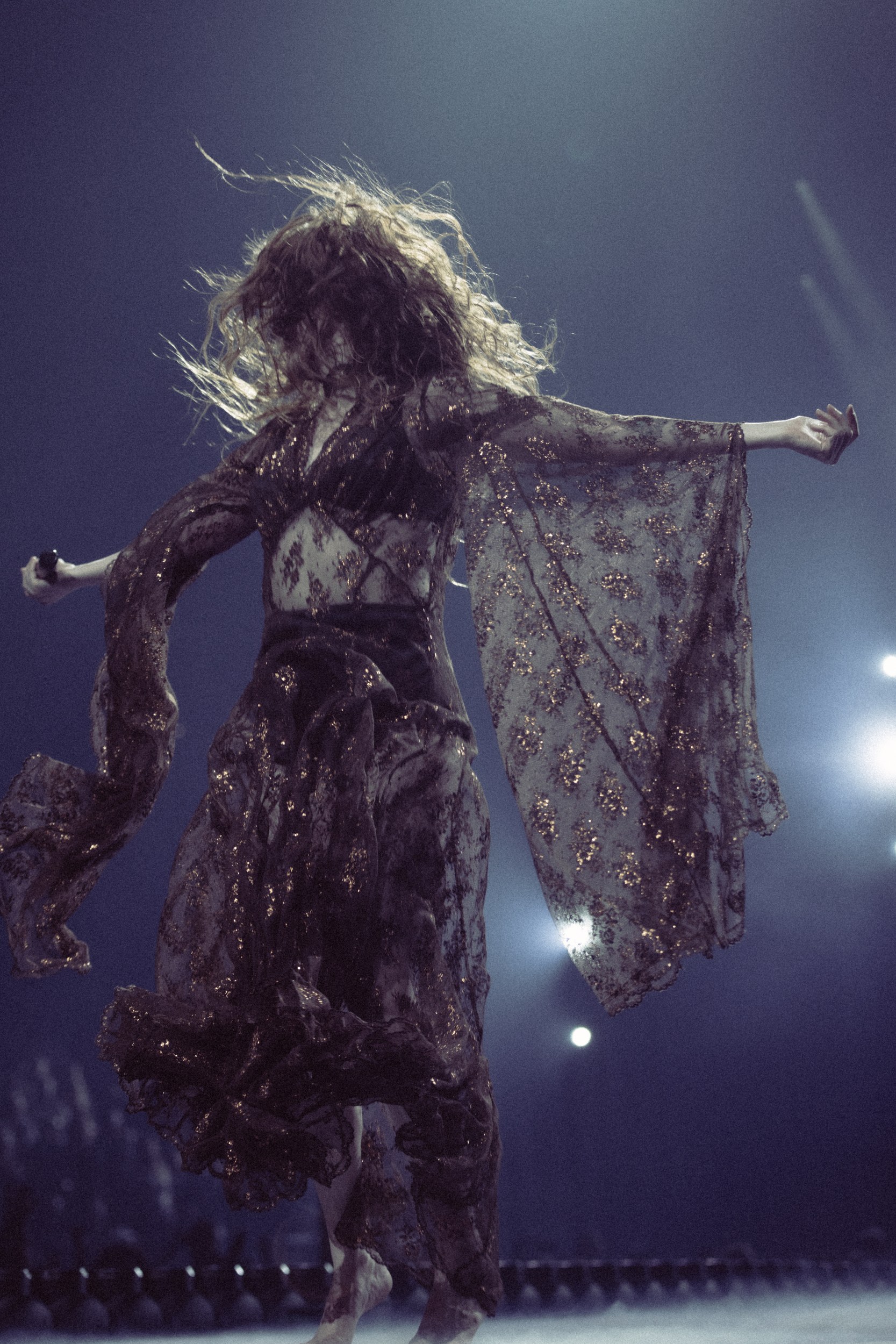 Performer in a flowing dress dances on stage, vibrant motion, spotlight shines.